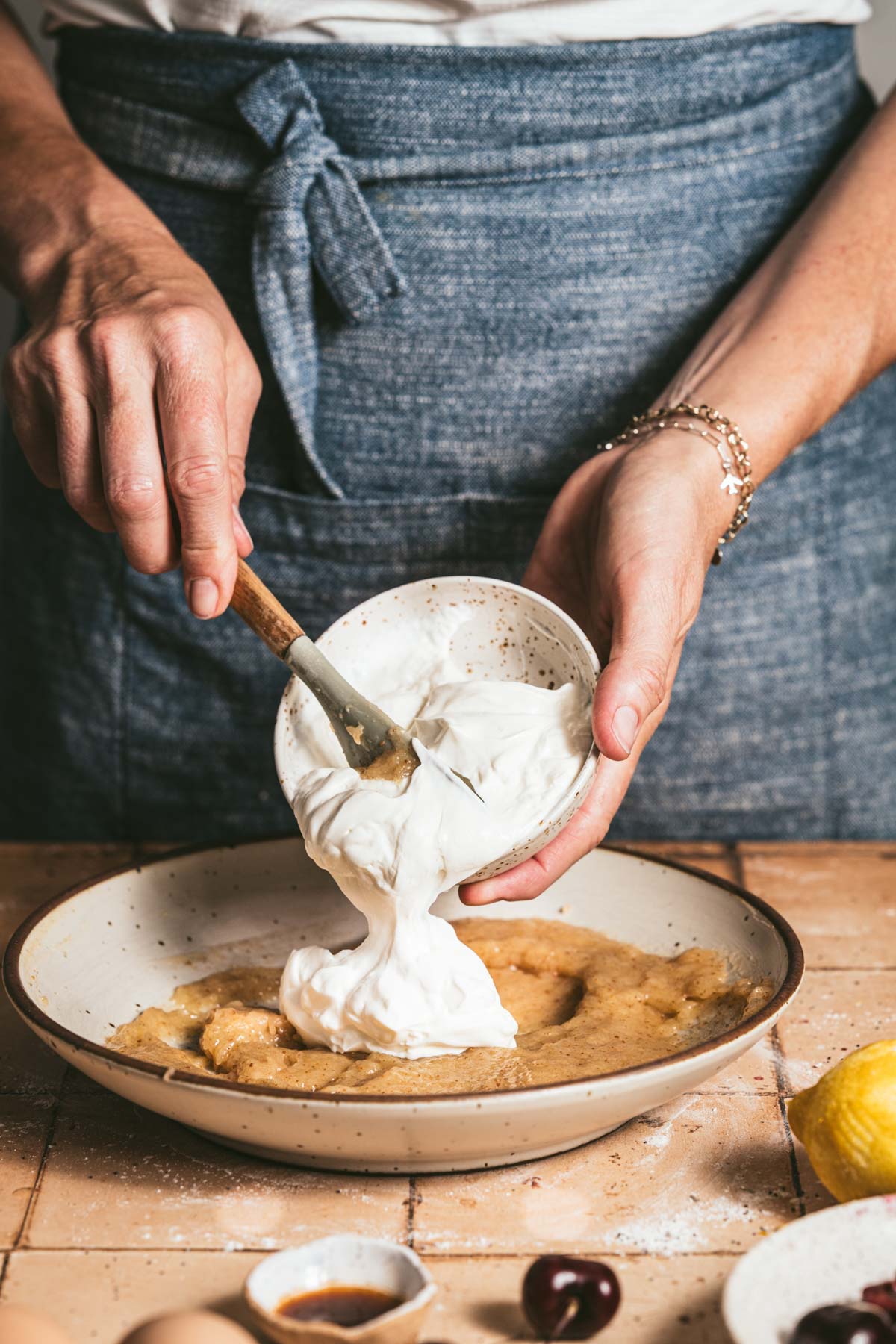 hands in frame adding sour cream to the batter