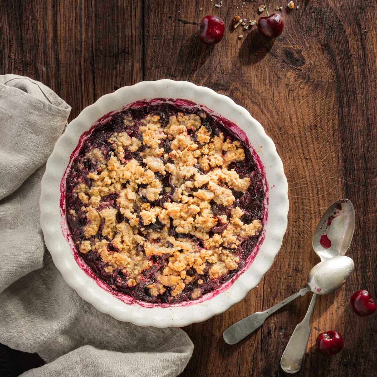 baked cherry crisp shown in a serving dish; wooden background