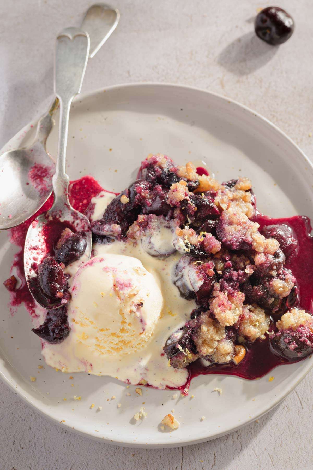 cherry crisp on a plate served with a scoop of ice-cream, two spoons