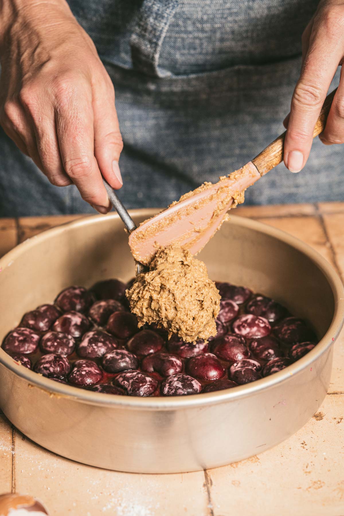 hands in frame scooping batter on top of the cherries