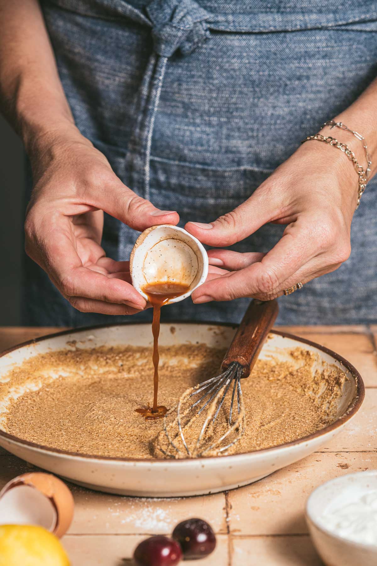hands in frame pouring vanilla and almond extract into the batter