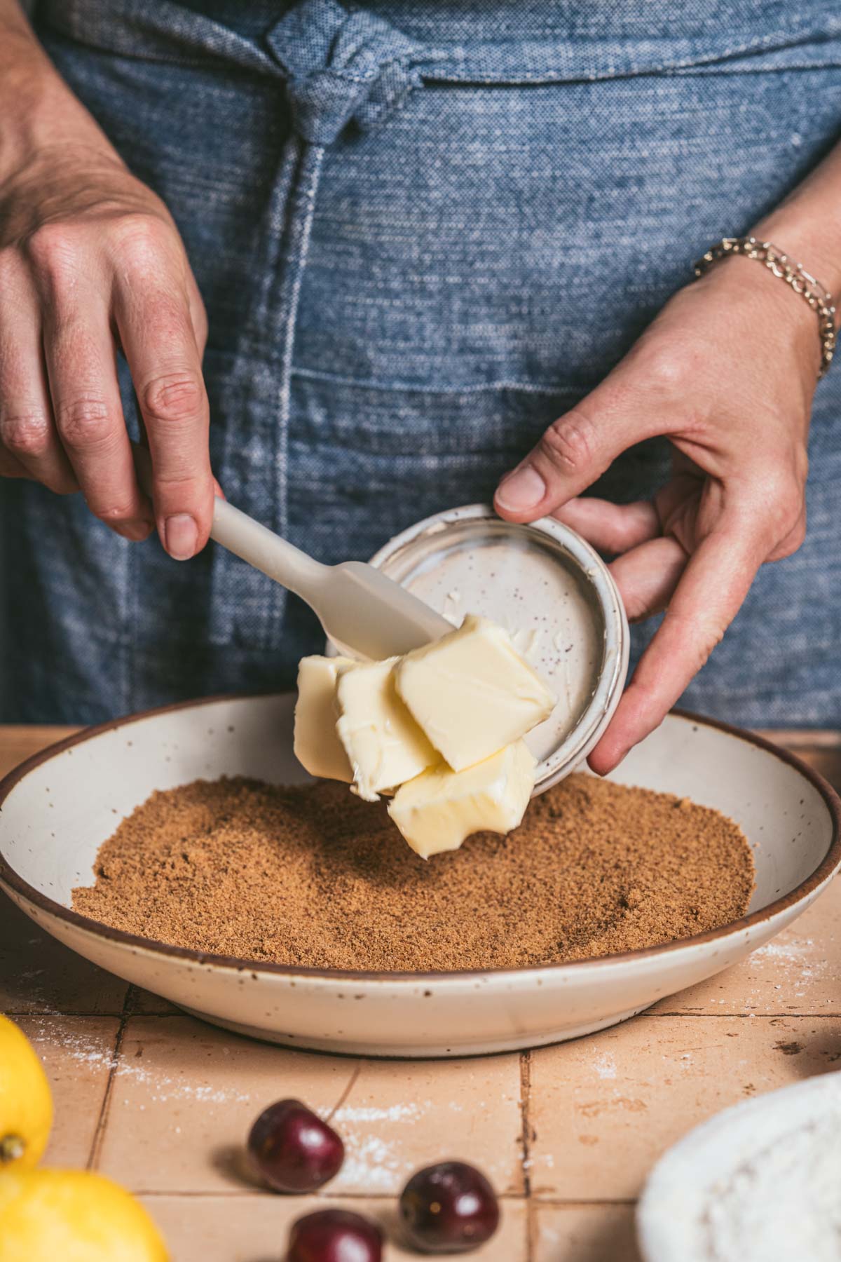 hands in frame scooping butter into a bowl with sugar