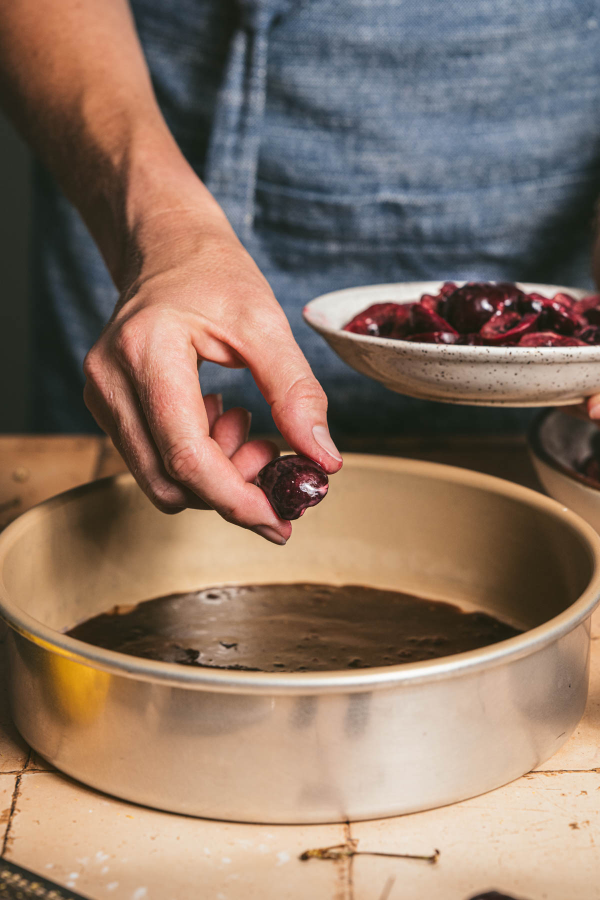 hands in frame holding cherries over a baking pan