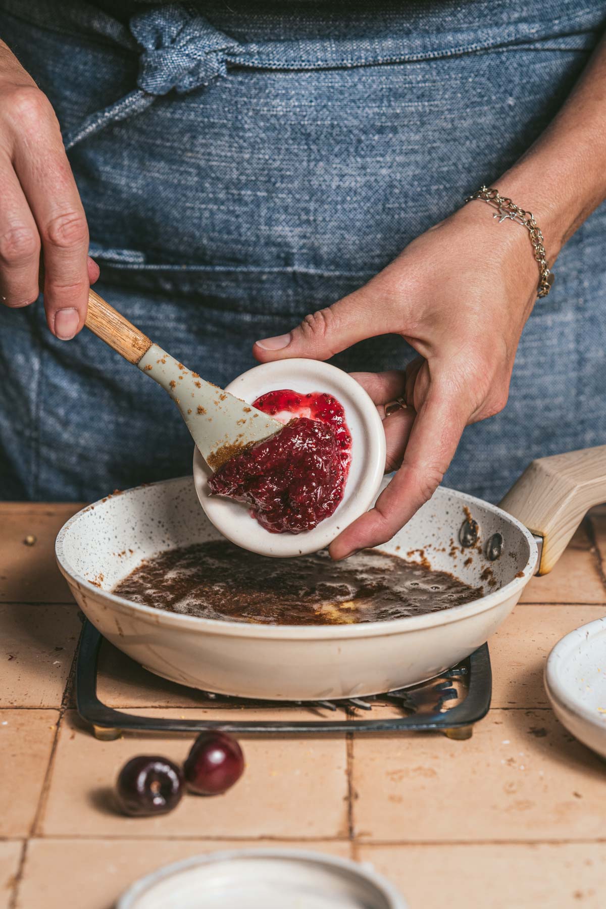 hands in frame scooping red currant jam into a pan