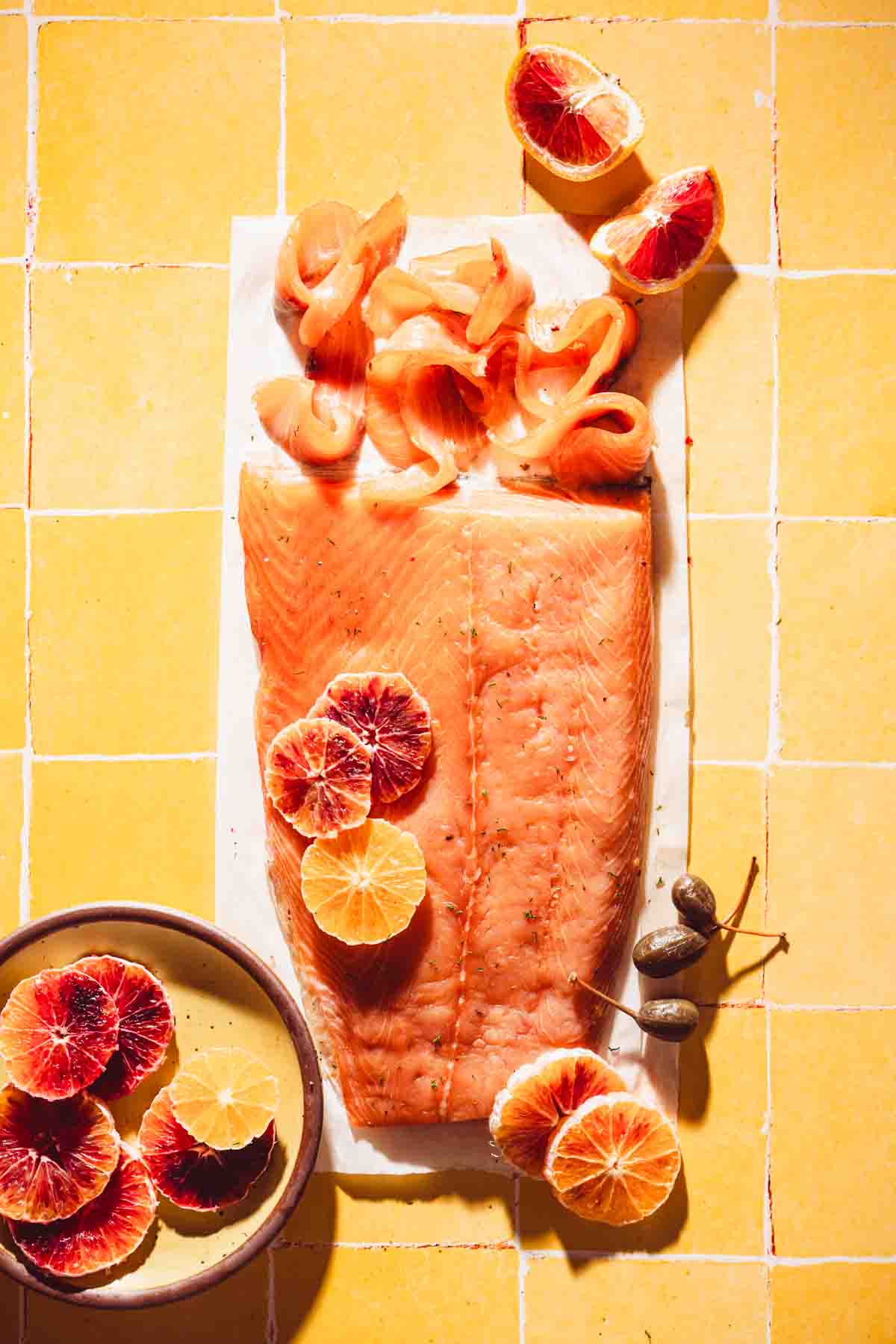 salmon on a piece of parchment paper, orange slices on a plate