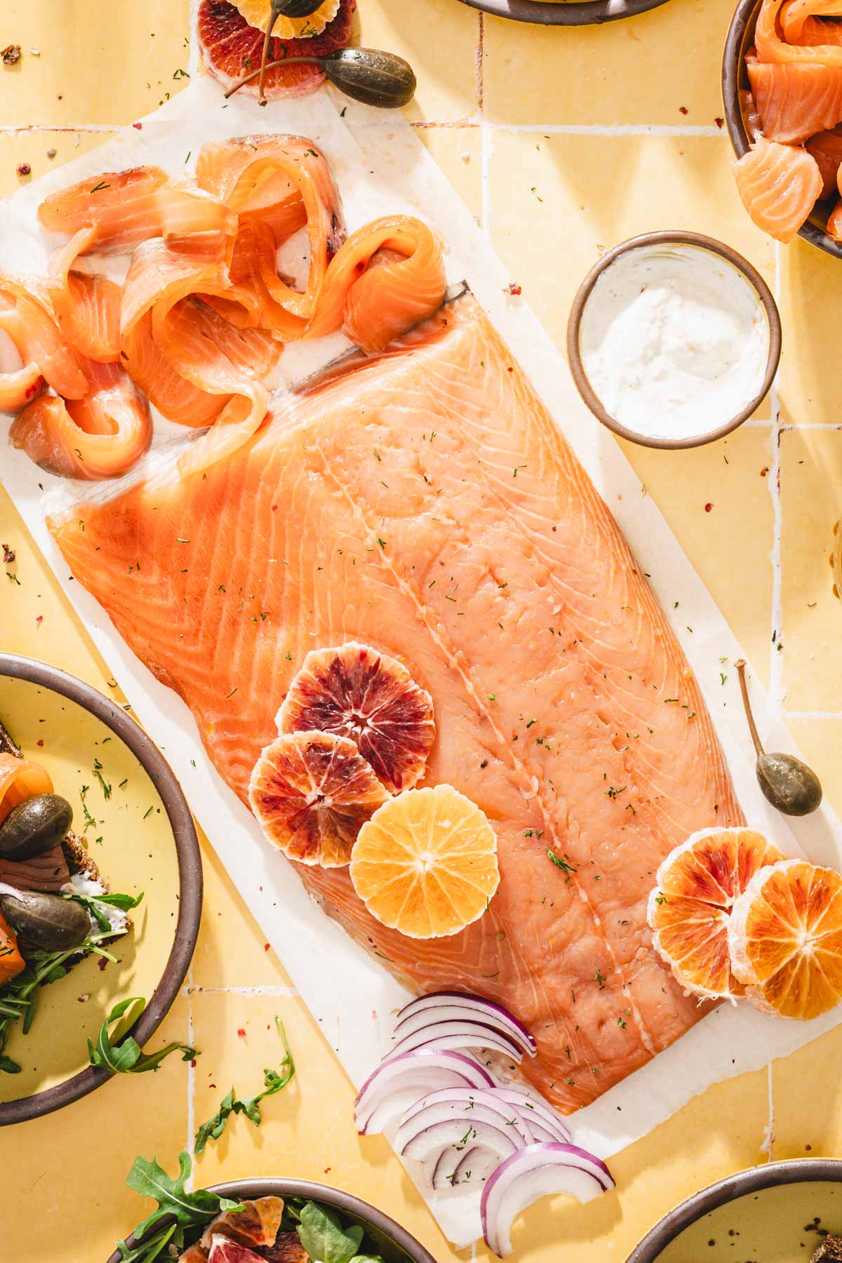 cured salmon on a parchment paper, some slices taken out, oranges, plate with salmon