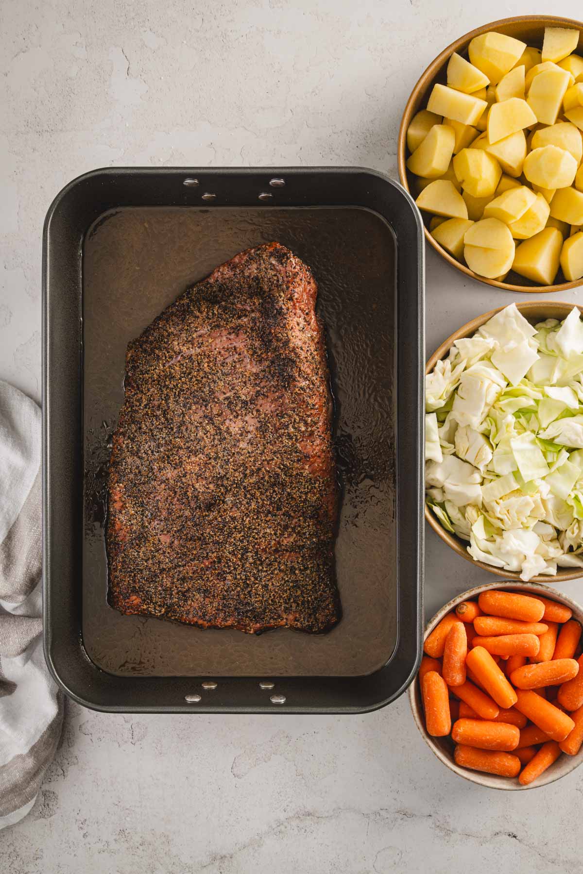 corned and smoked brisket in a roasting pan filled with liquid, bowls with veggies to the side