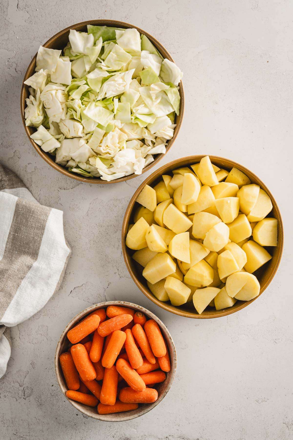 bowls with chopped cabbage, potatoes and carrots