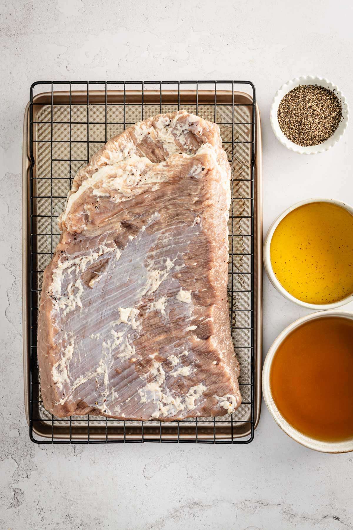 raw corned brisket on a drying rack, bowl with brine to the side, bowl with seasoning