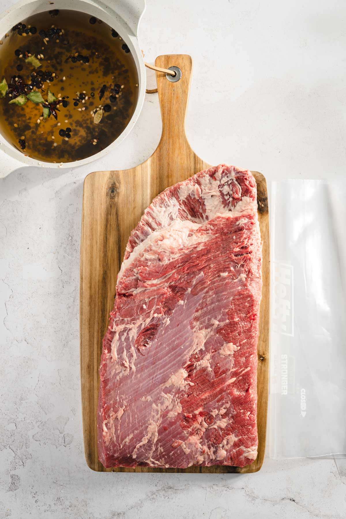 whole raw brisket on the cutting board, after trimming and small pot with the brine liquid