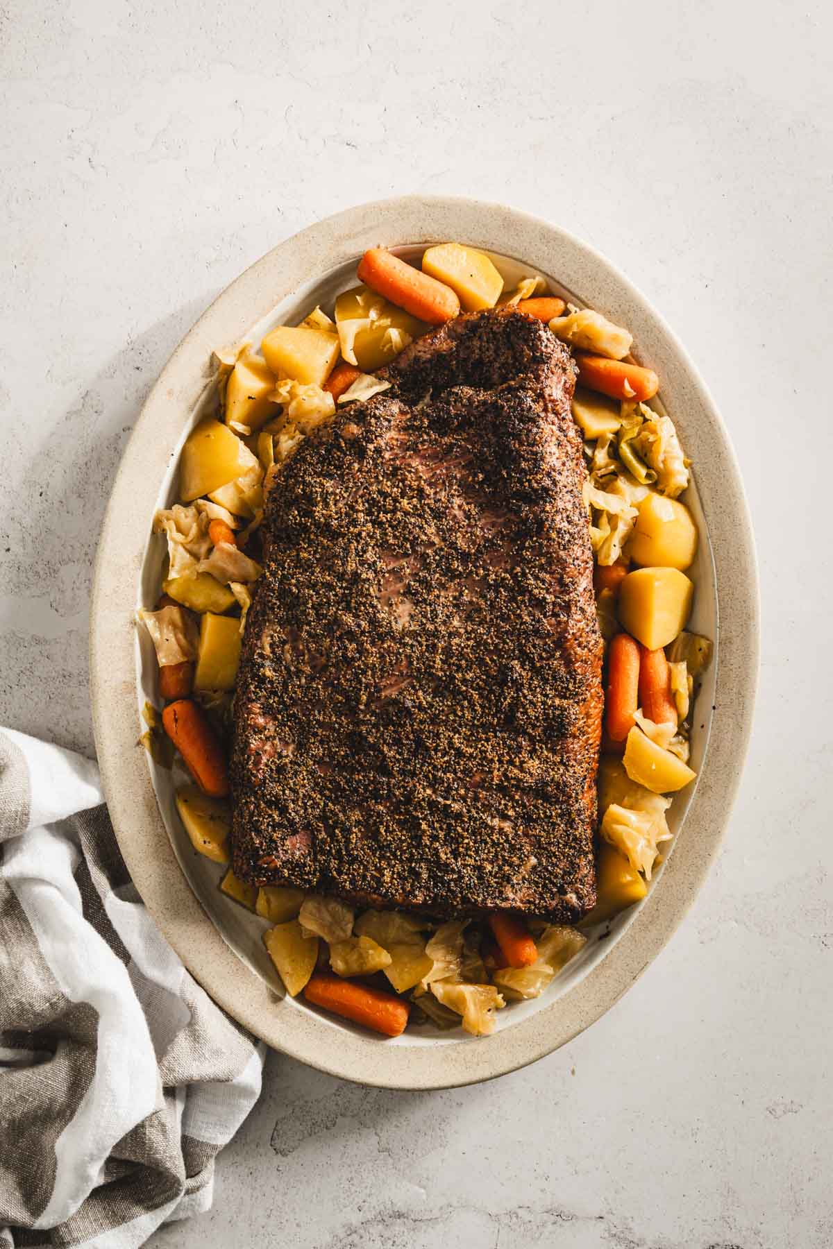 cooked corned beef brisket on a serving platter with cooked veggies underneath and to the side