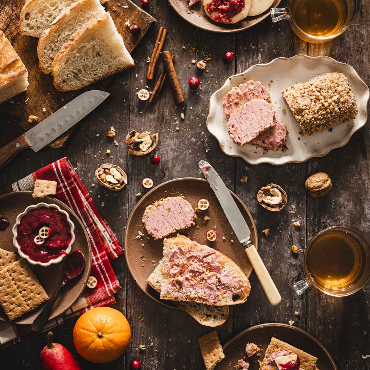 top view, slices of bread with cran butter on a plate; small plate with the butter roll, plate with dish with cran sauce, orange and pear on the side