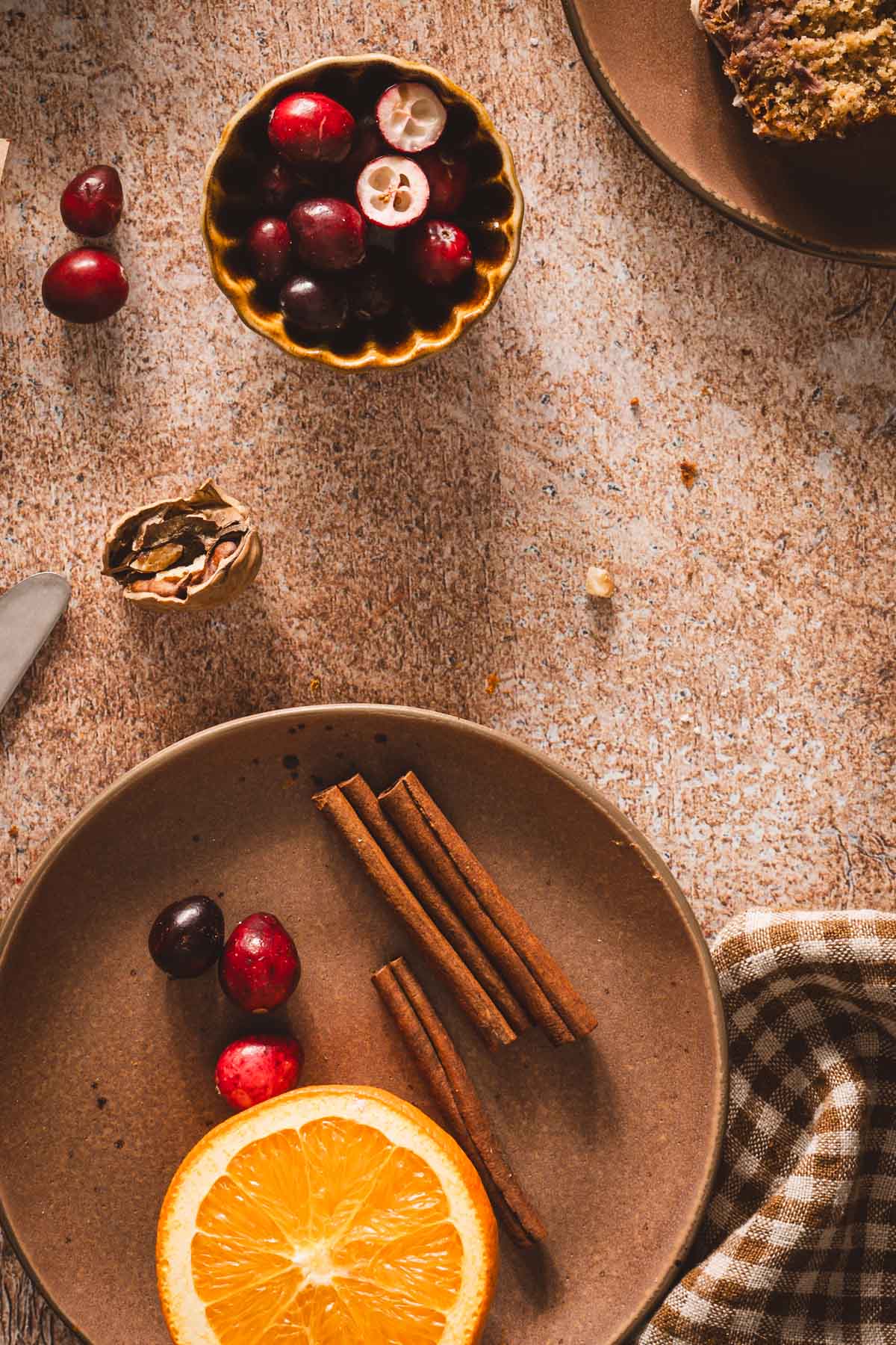 plate with cinnamon sticks, fresh cranberries and half of an orange