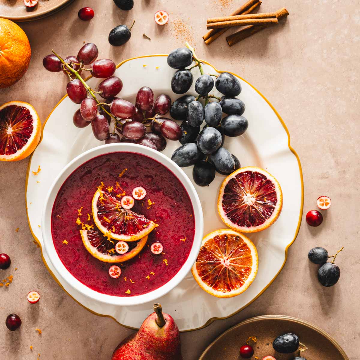 bowl with cranberry sauce on a lager plate, grapes, oranges, cinnamon sticks, plates with fresh fruit, pears