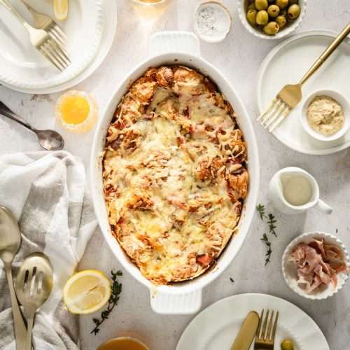 Croissant Bake in a serving dish, plates around, utensils, dish with honey, ham and sauce, glasses with tea