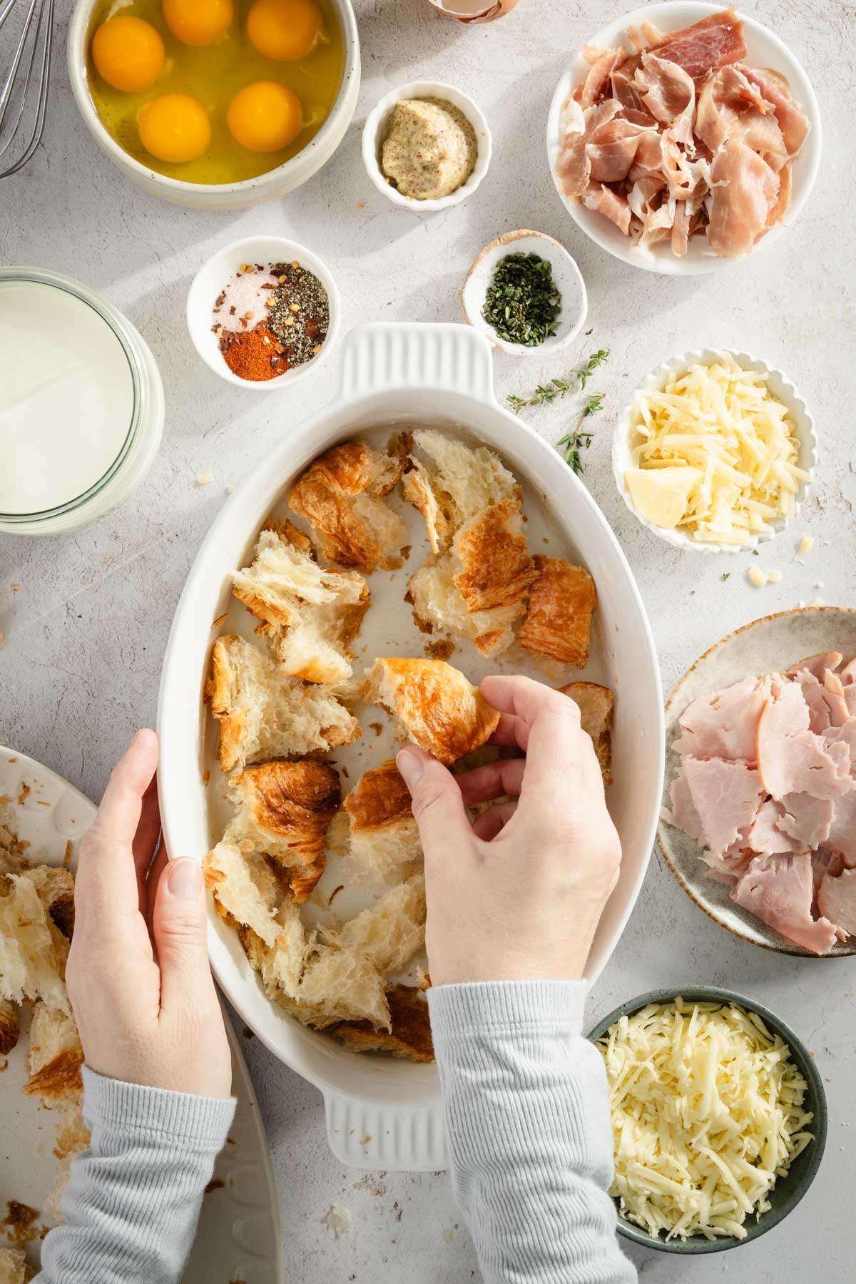 hands in frame adding torn croissant to the baking dish