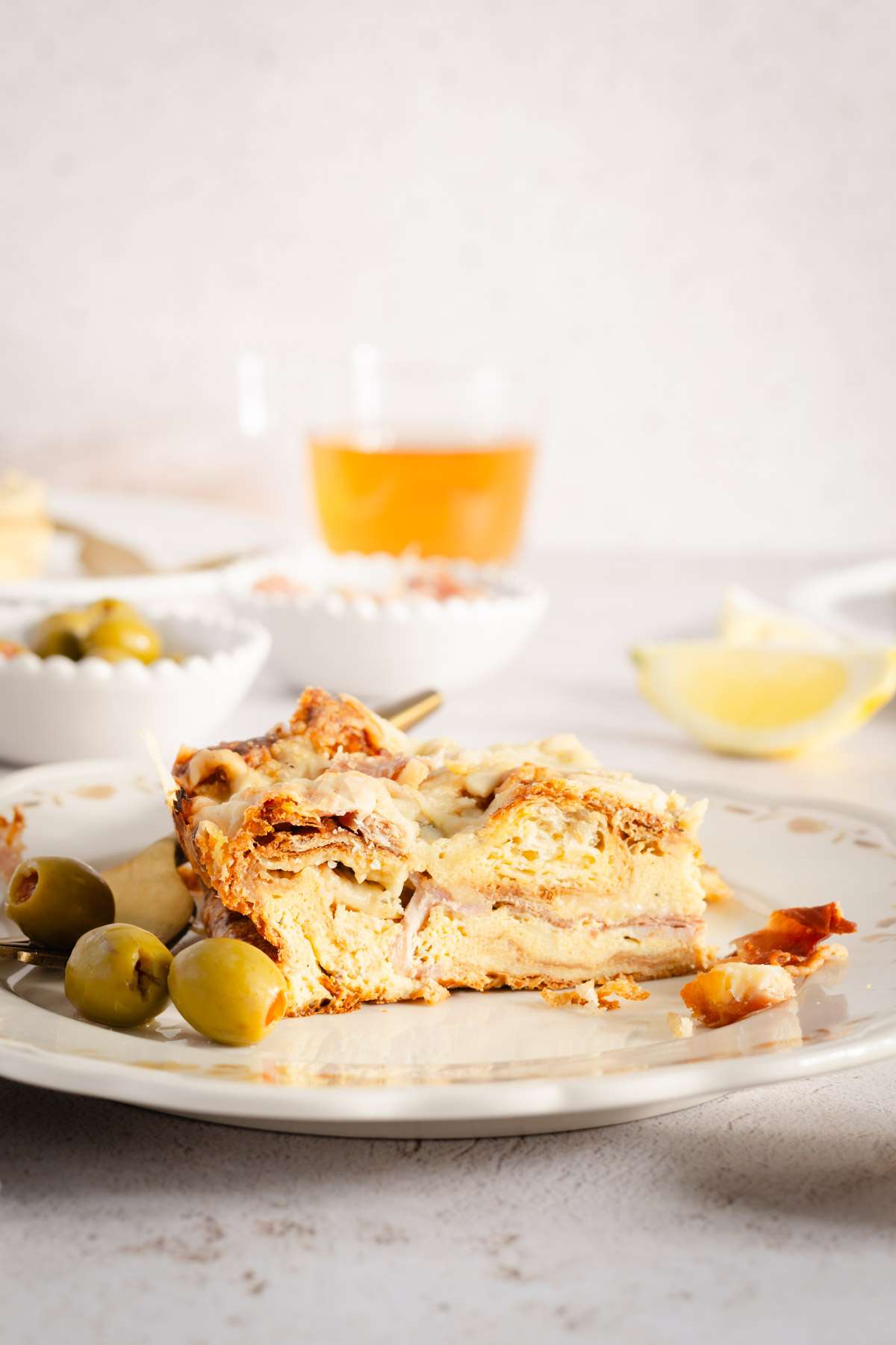 slice of croissant bake on a plate, dishes with olives, sauce, glass with tea