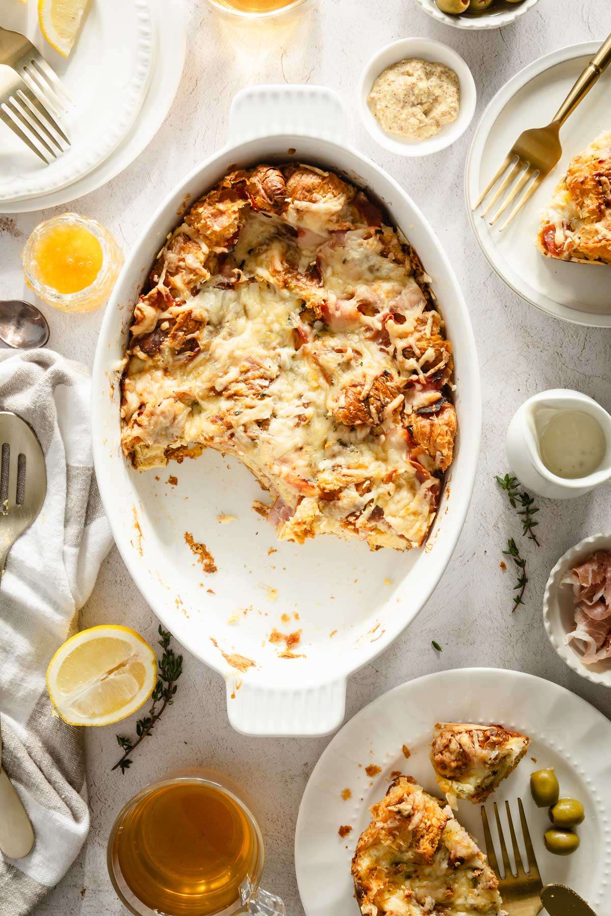 Croissant Bake in a serving dish, plates around, utensils, dish with honey, ham and sauce, glasses with tea