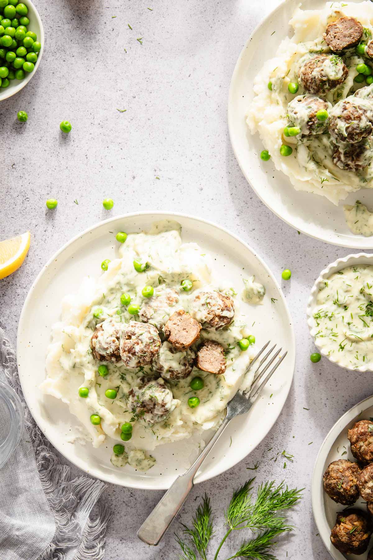 serving plates with dill meatballs over mashed potatoes, green peas and dill sauce