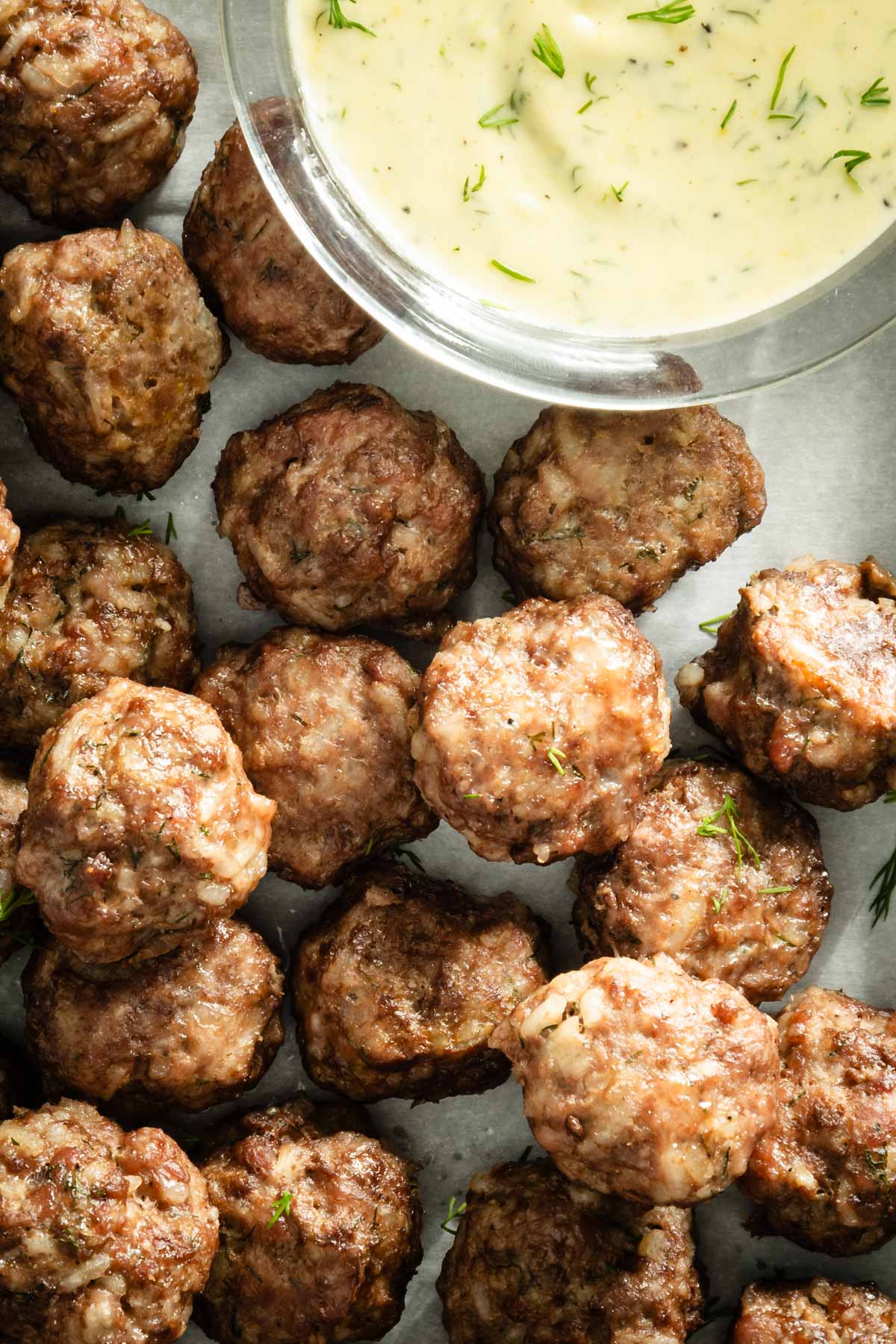 close up of meatballs on a baking sheet, dipping sauce to the side