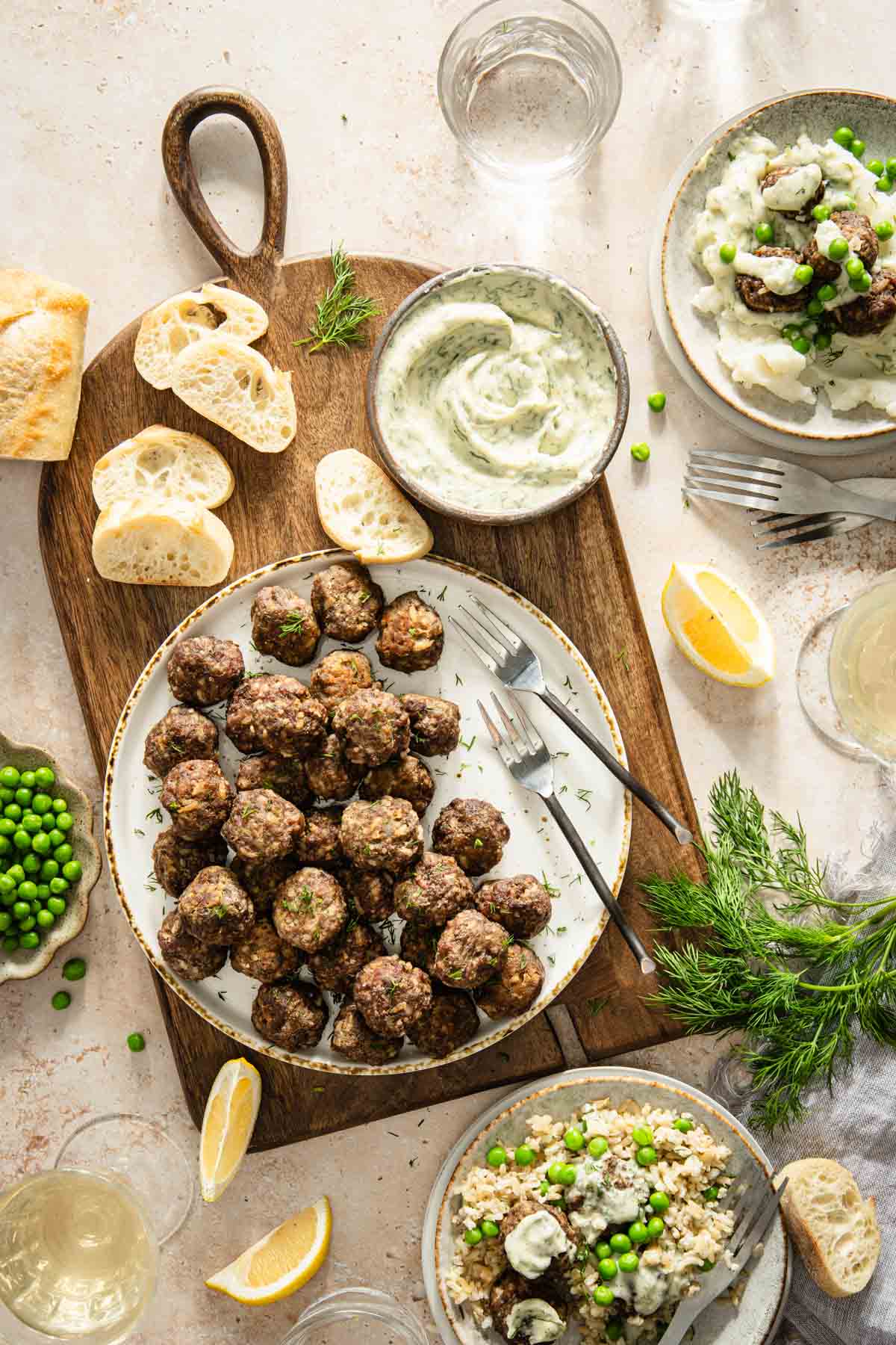 dill meatballs on a plate served on a woode board, slices of bread, dish with sauce, lemon wedges, fresh dill, green peas