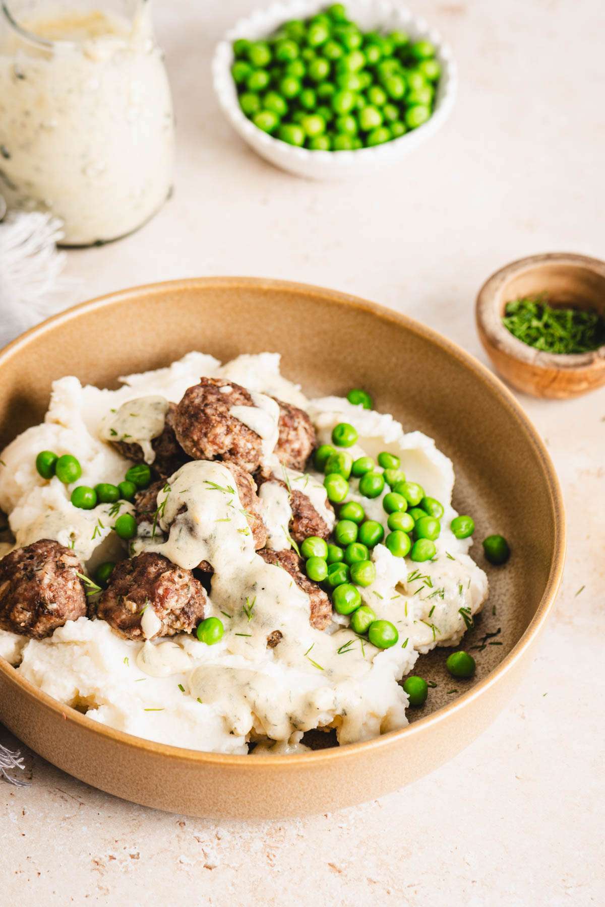 bowl with mashed potatoes with meatballs, sauce and green peas