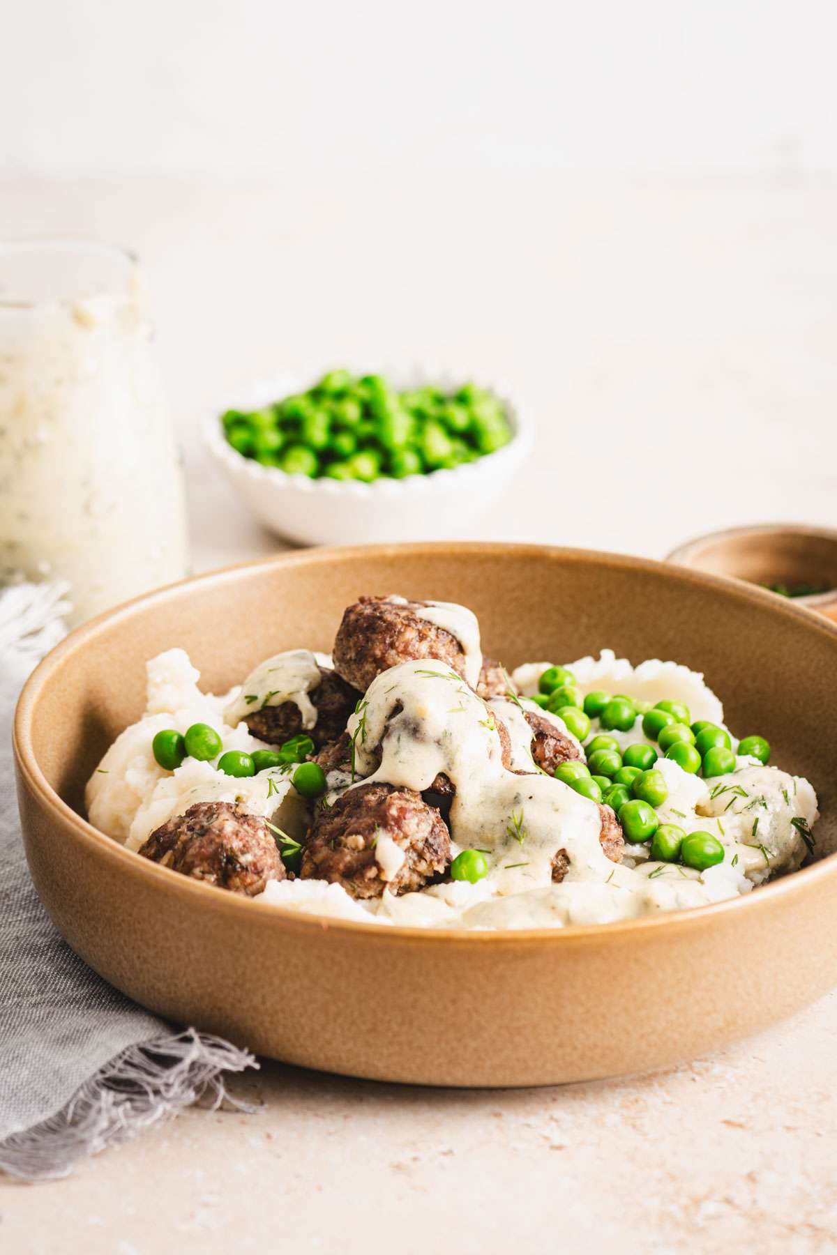 bowl with mashed potatoes with meatballs, sauce and green peas