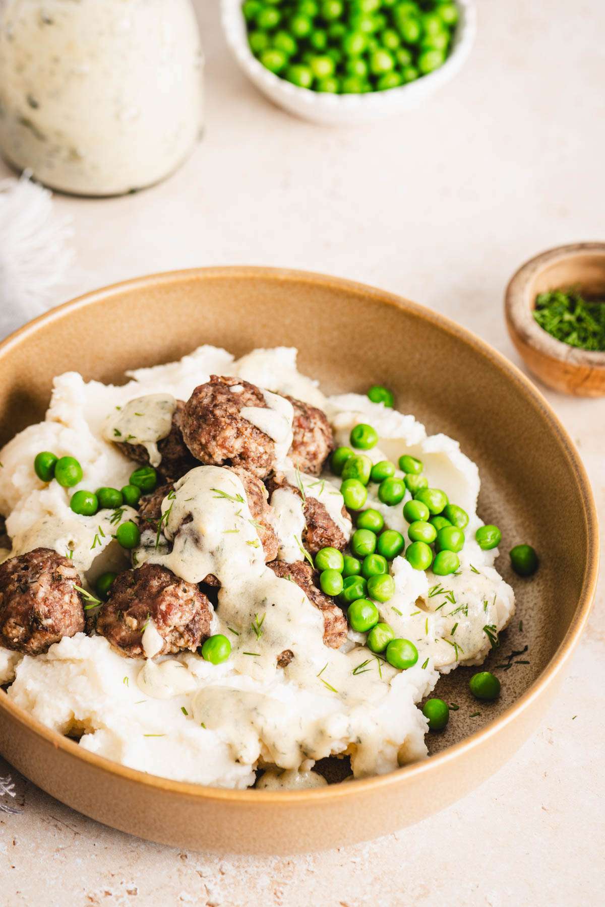 bowl with mashed potatoes with meatballs, sauce and green peas