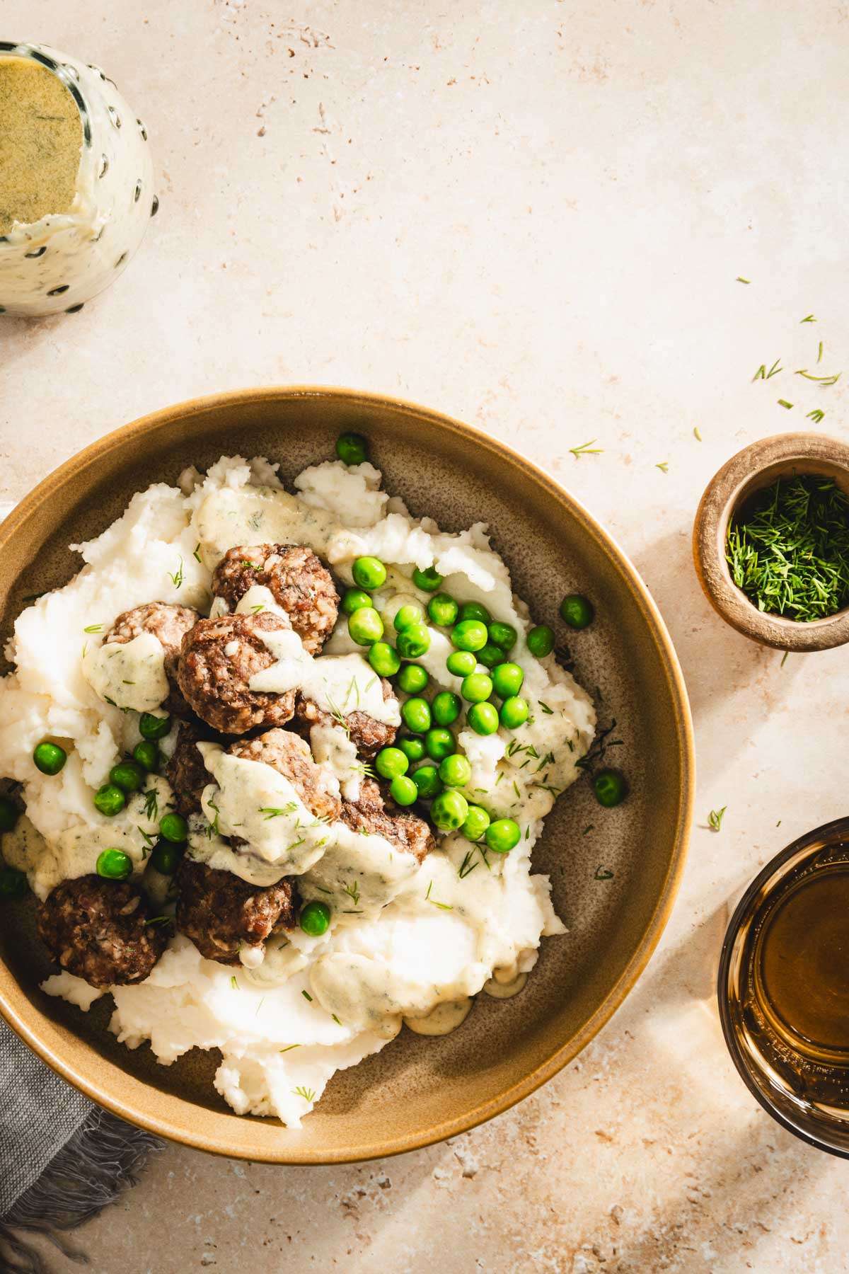 bowl with mashed potatoes with meatballs, sauce and green peas, top view