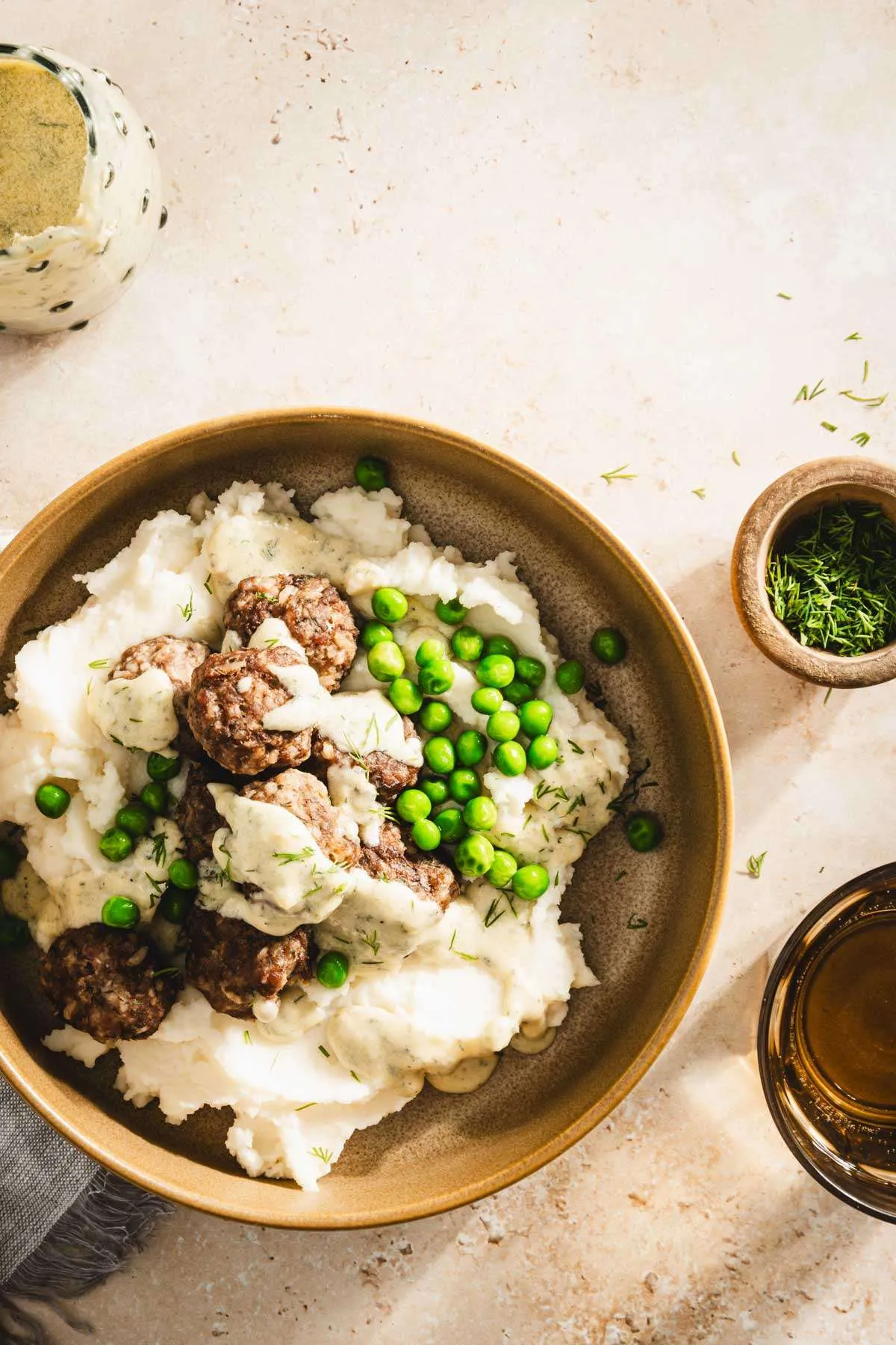 bowl with mashed potatoes with meatballs, sauce and green peas, top view