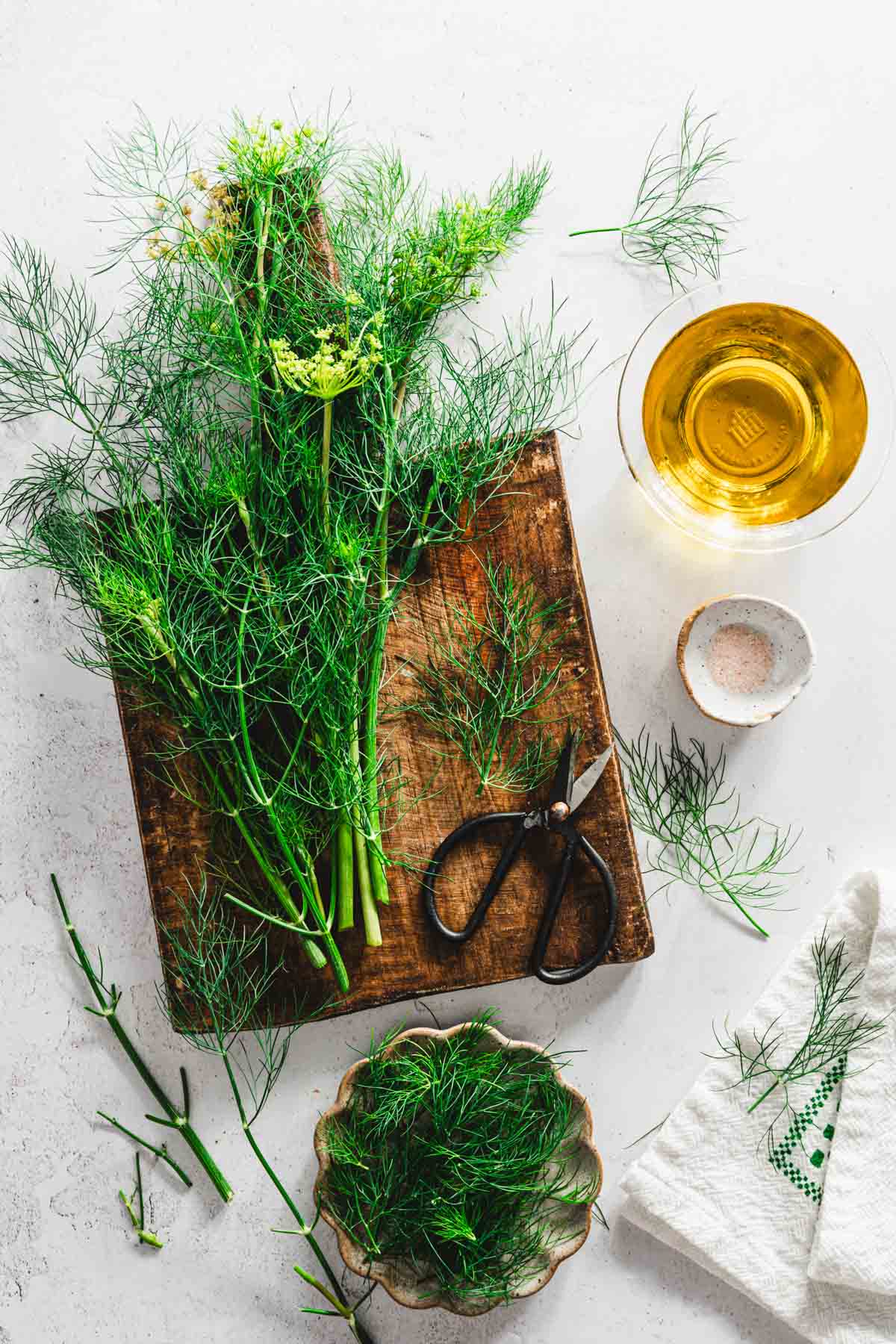 bunch of fresh dill on a wooden cutting board, dish with oil and salt,