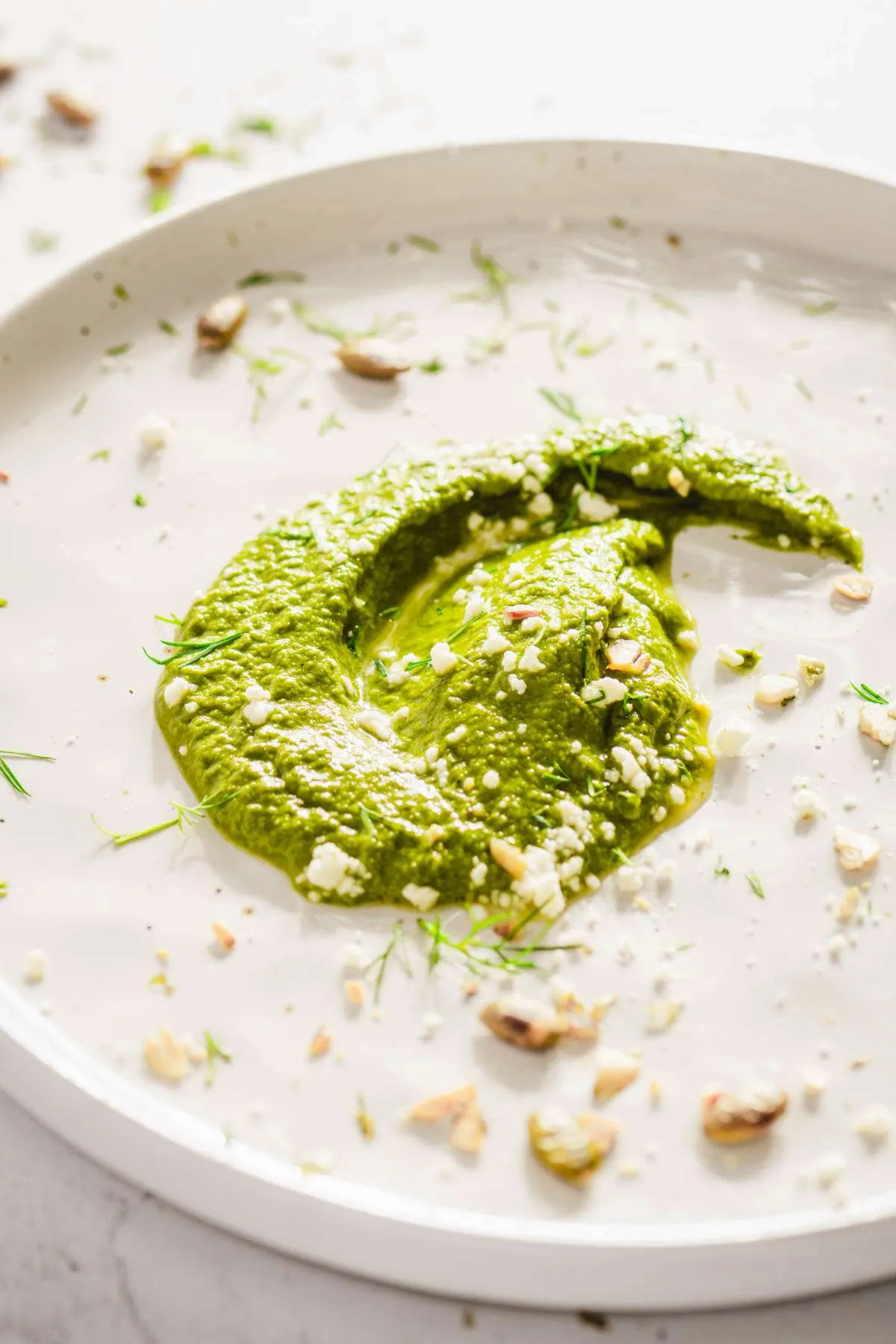 a dollop of dill pesto on a plate, garnished with crushed pumpkin seeds, chopped dill, 3/4 view