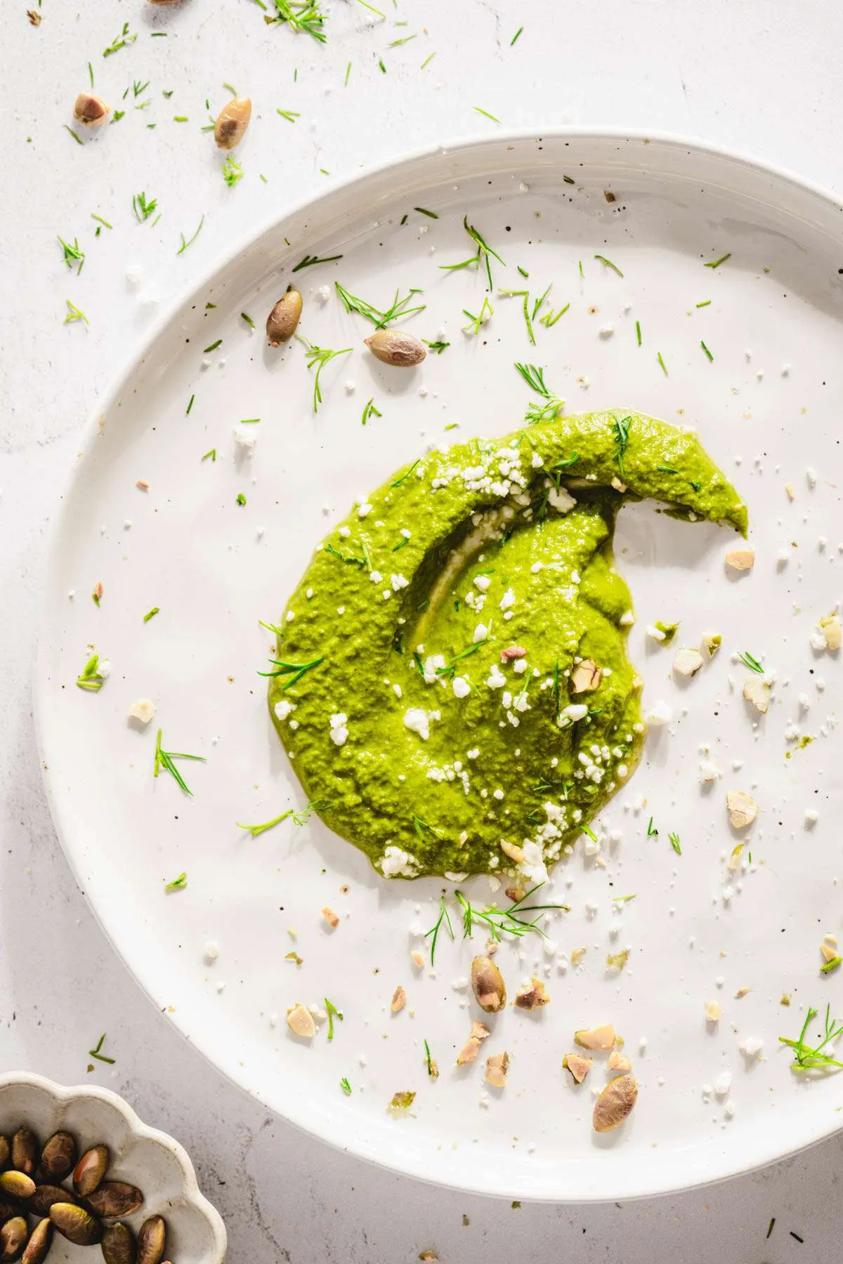 a dollop of dill pesto on a plate, garnished with crushed pumpkin seeds, chopped dill, top view