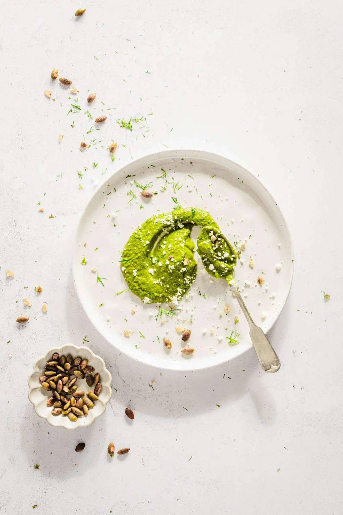 made pesto spread on a plate, spoon and small dish with pumpkin seeds