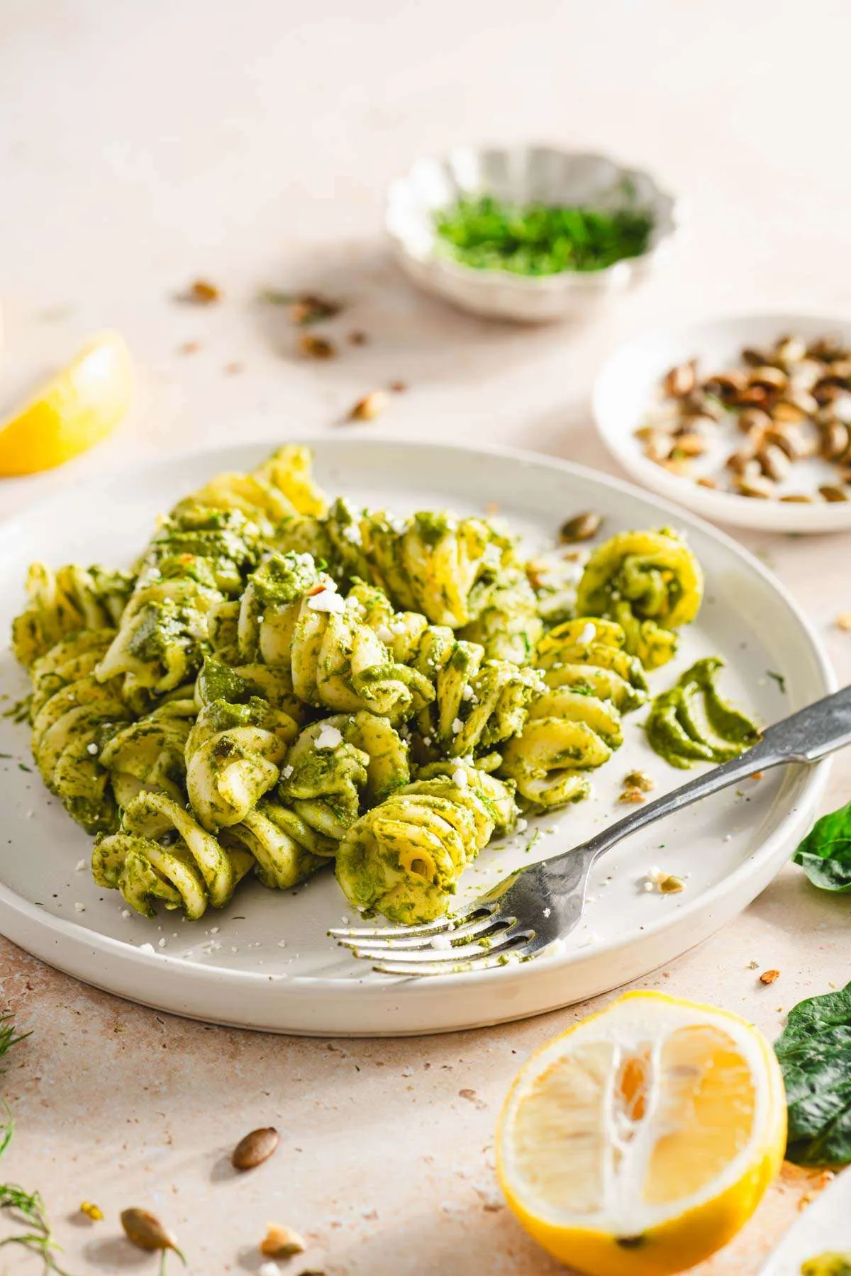 close up of pesto pasta, dish with pumpkin seeds and fresh dills, lemon wedges