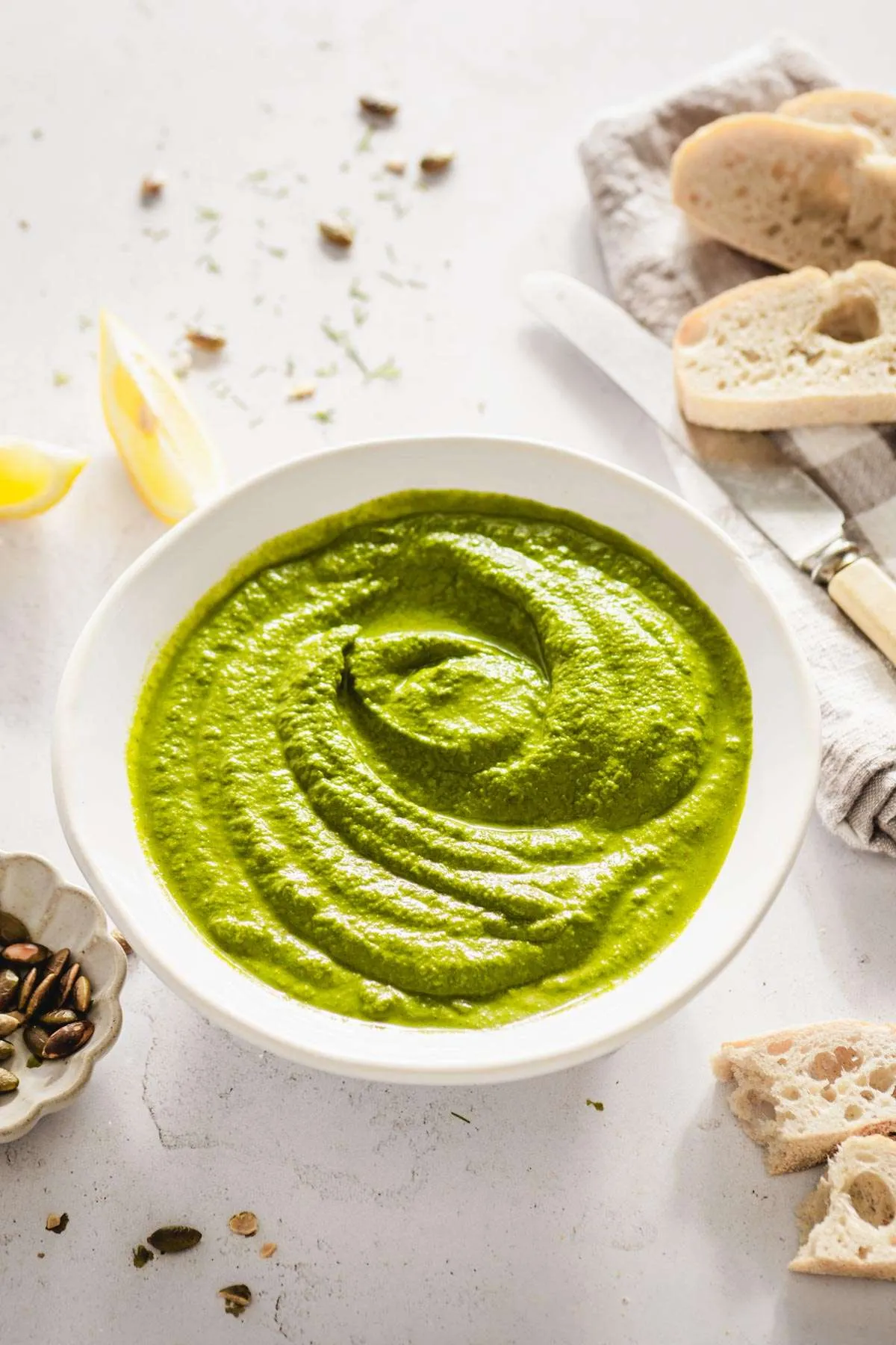bowl with dill pesto, lemon wedges, bread slices, butter knife, dish with pumpkin seeds