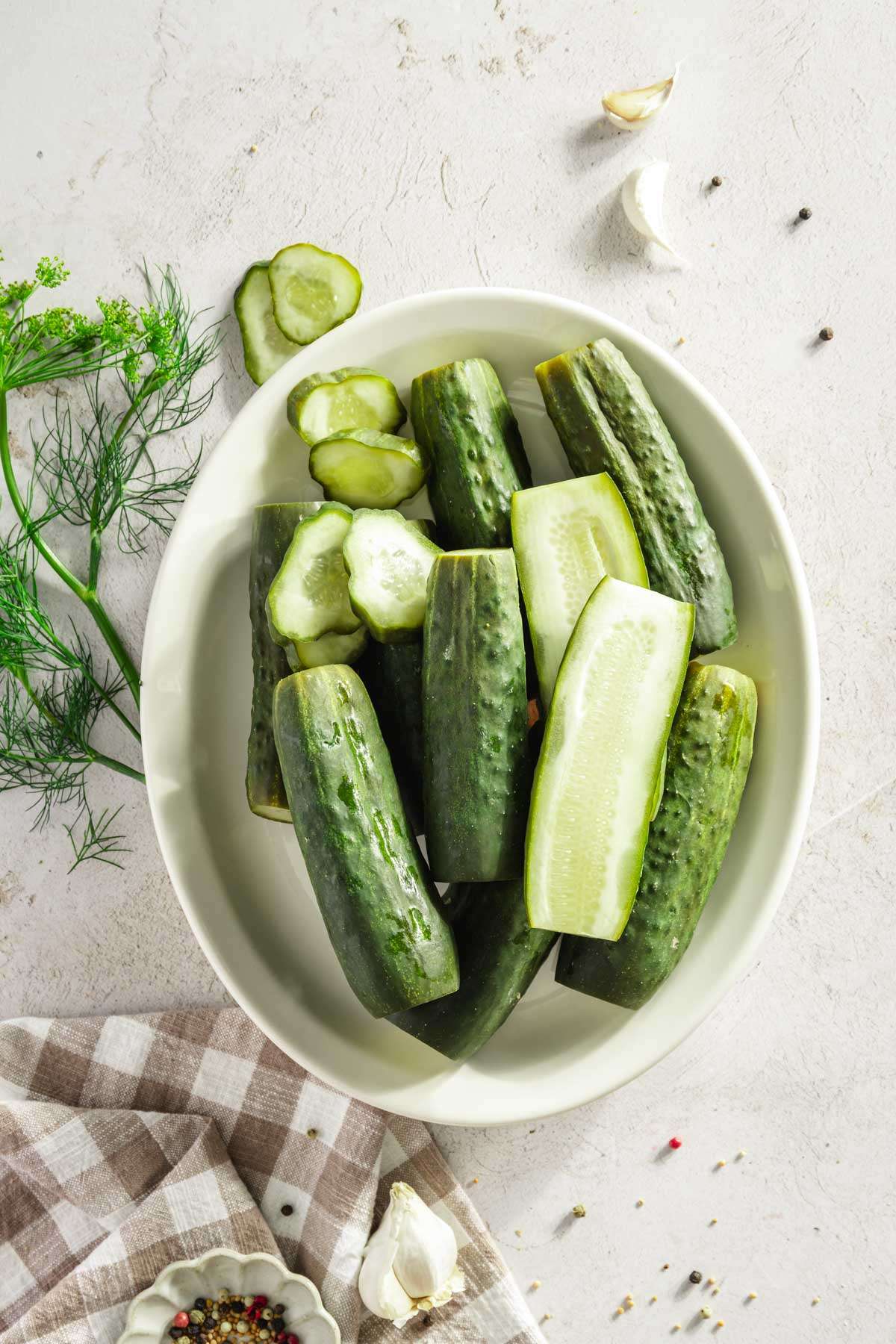 larger plate with half sour pickles arranged on it, fresh dill, some pickled cut into halves, some sliced