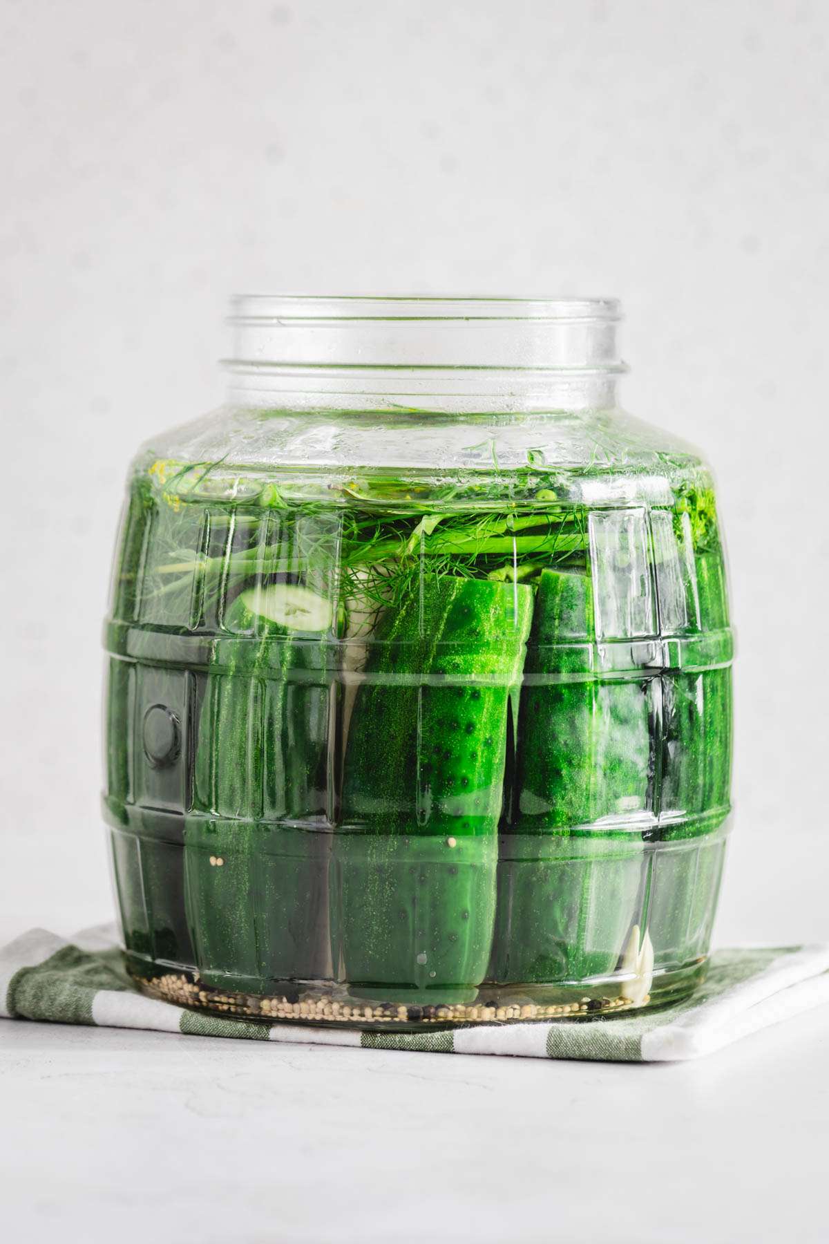 large glass jar with pickling cucumbers arranged inside, front view