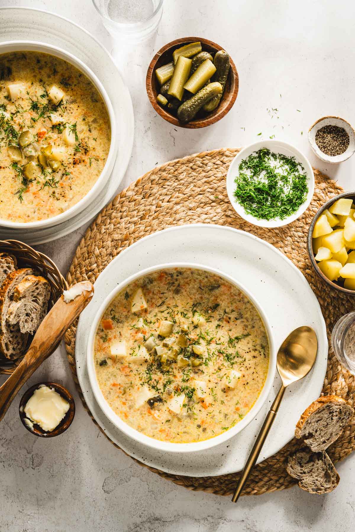 dill pickle soup in a serving bowls, , pickles, dill, potatoes, bread around