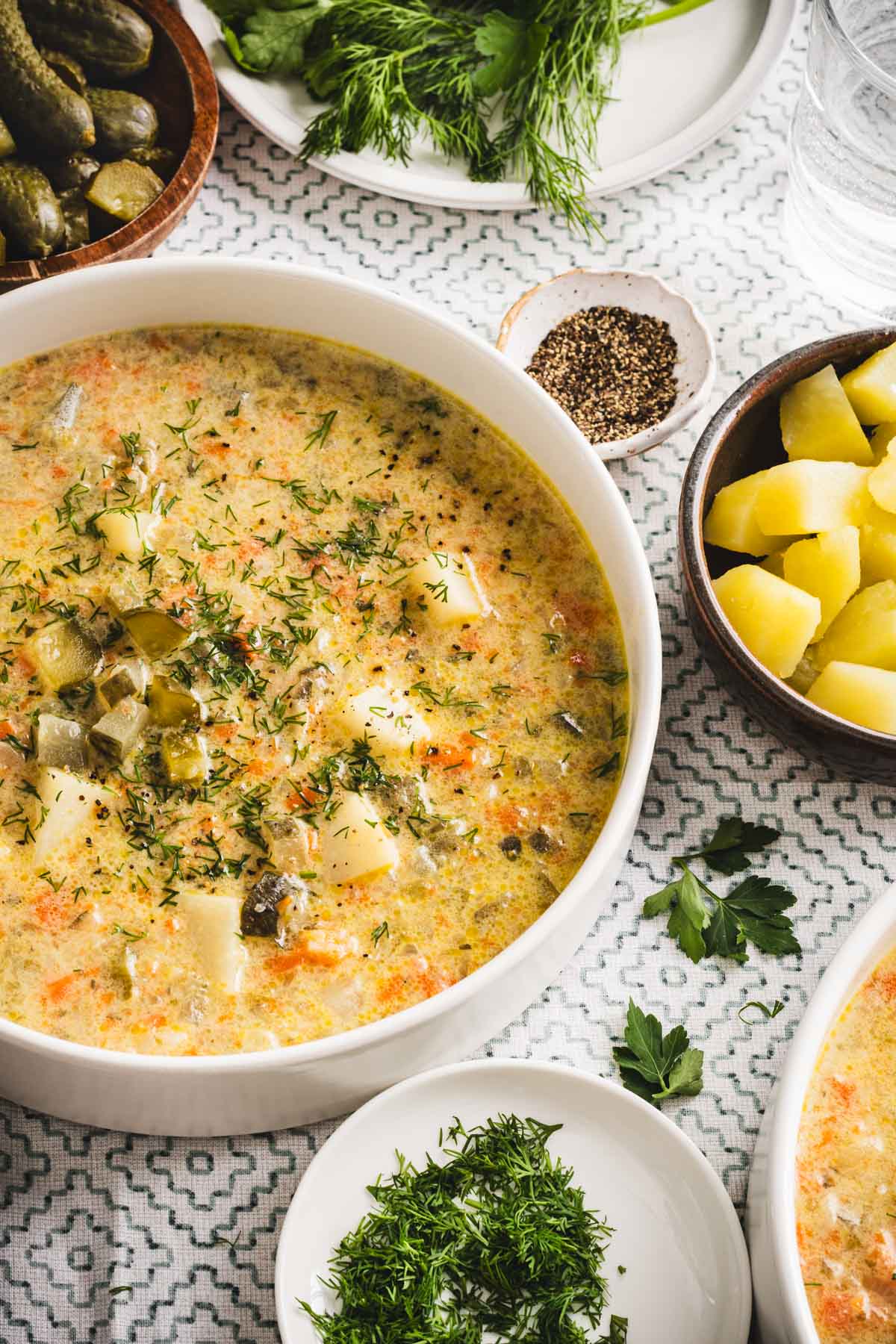 dill pickle soup in a serving bowls, , pickles, dill, potatoes, bread around