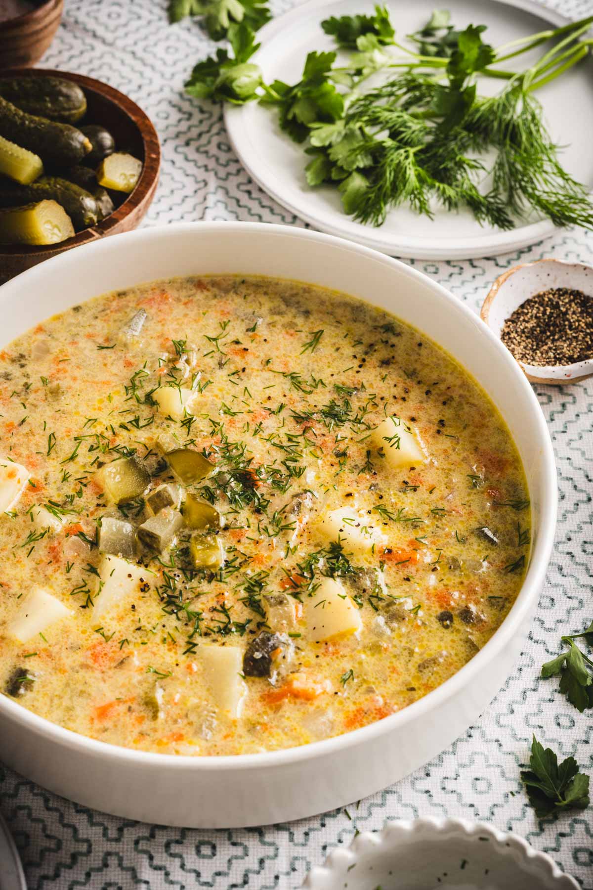 dill pickle soup in a serving bowls, , pickles, dill, potatoes, bread around