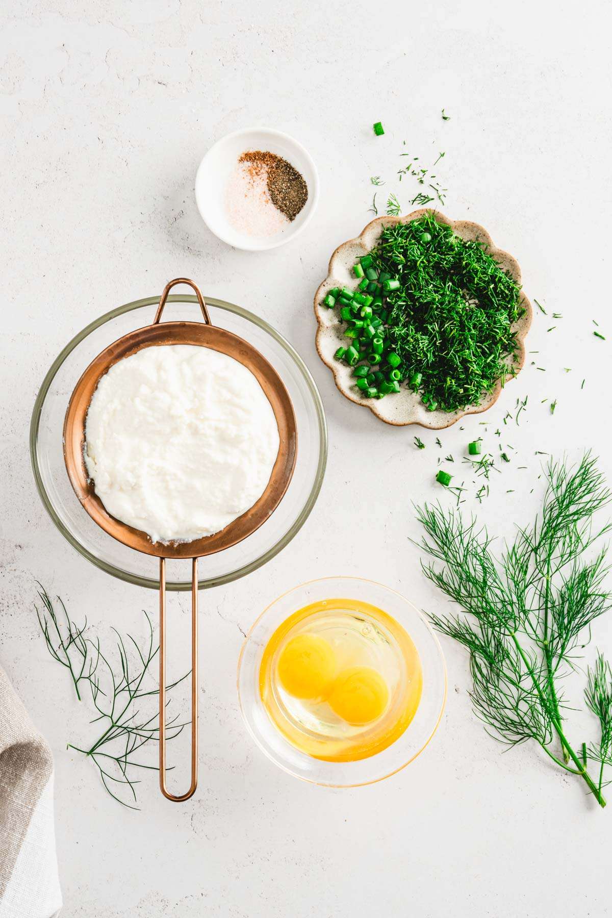 ricotta cheese on a strainer, dish with salt, chopped dill and eggs