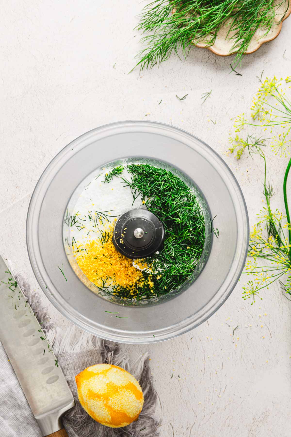 food processor container with all the ingredients to make dill salt, knife, lemon