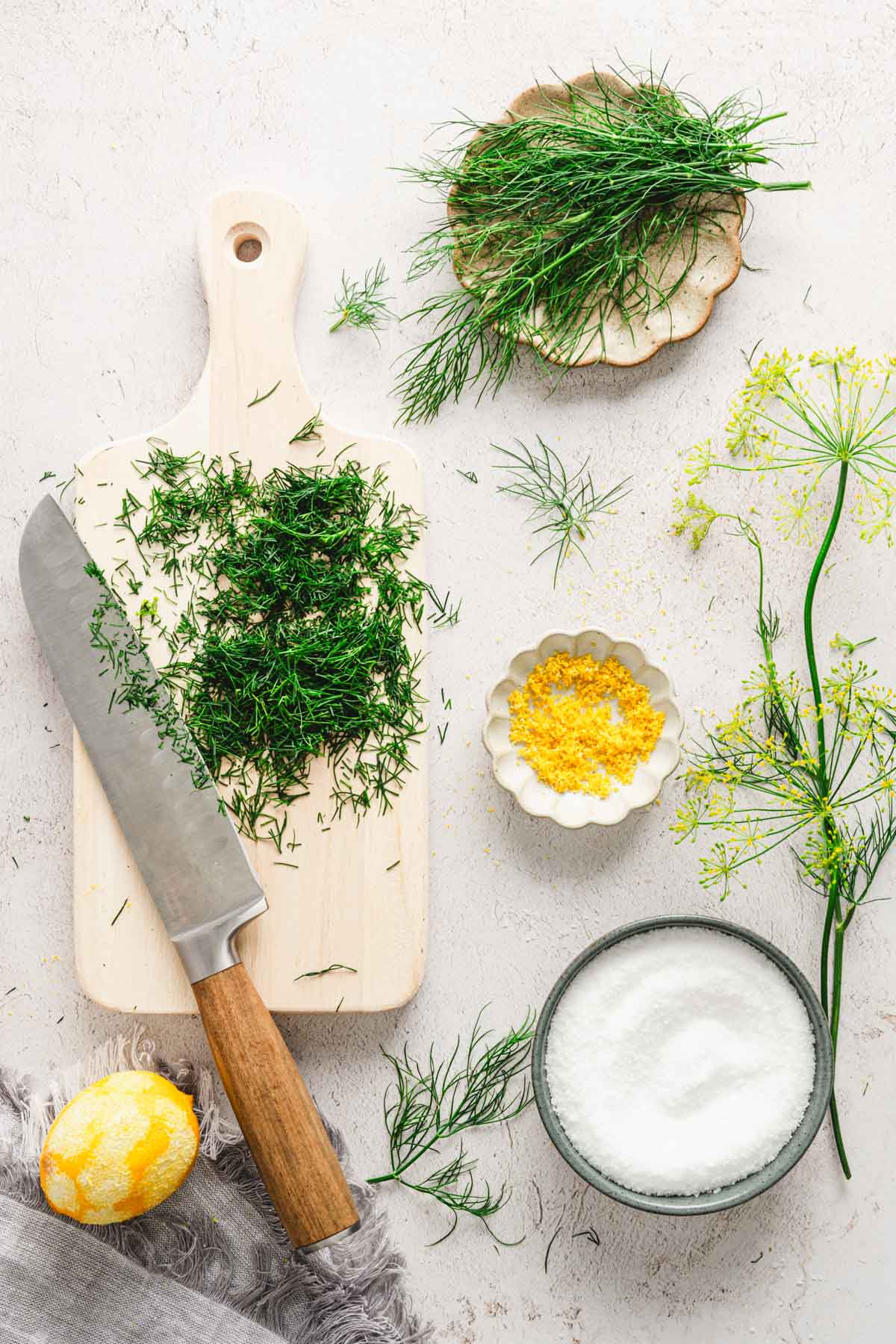 cutting board with chopped dill, large knife, dish with salt, lemon zest, one lemon