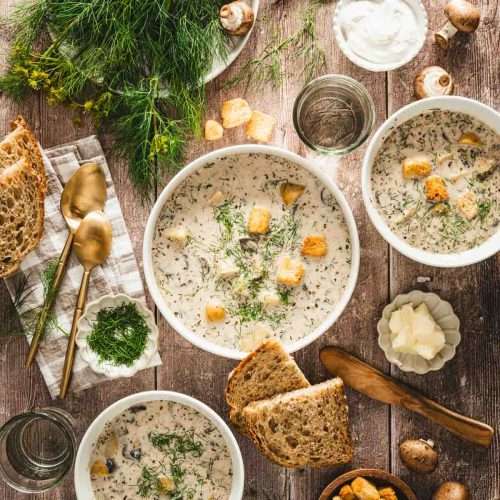 zupa koperkowa in a serving bowl, napkin, utensils, plate with butter, rustic bread, big bunch of dill,