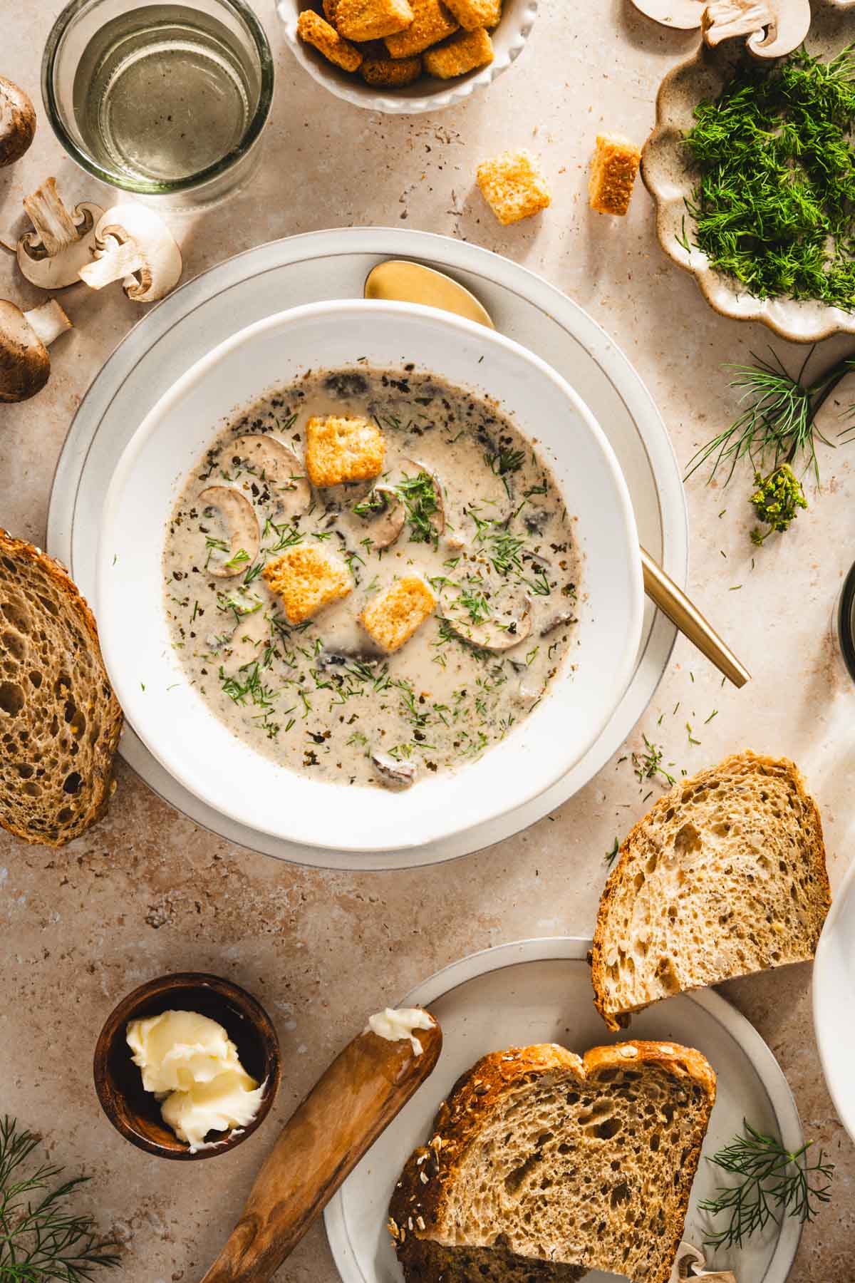 top view of dishes filled with zupa koperkowa, glasses with water, fresh dill, crusty bread