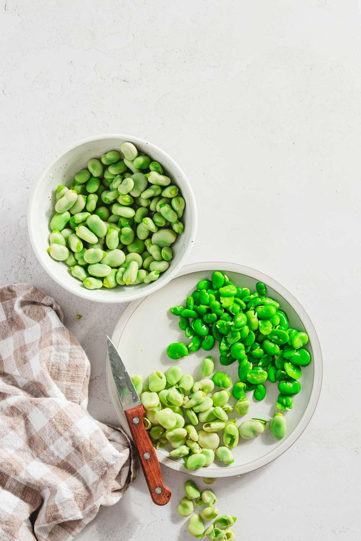 plate with blanched fava beans, some shelled ones , small knife