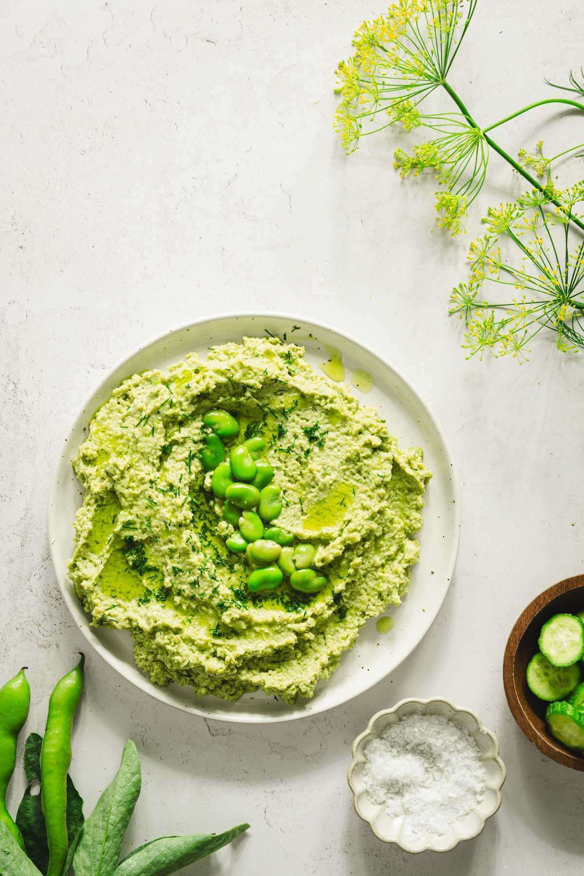 plate with fava bean hummus, dish with sliced cucumbers, salt, fresh dill