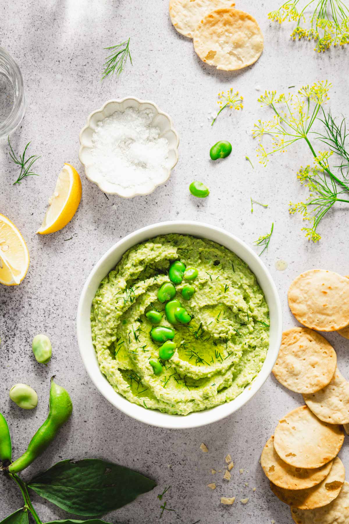 bowl with fava bean hummus, salt, lemon wedges, crackers, fresh dill