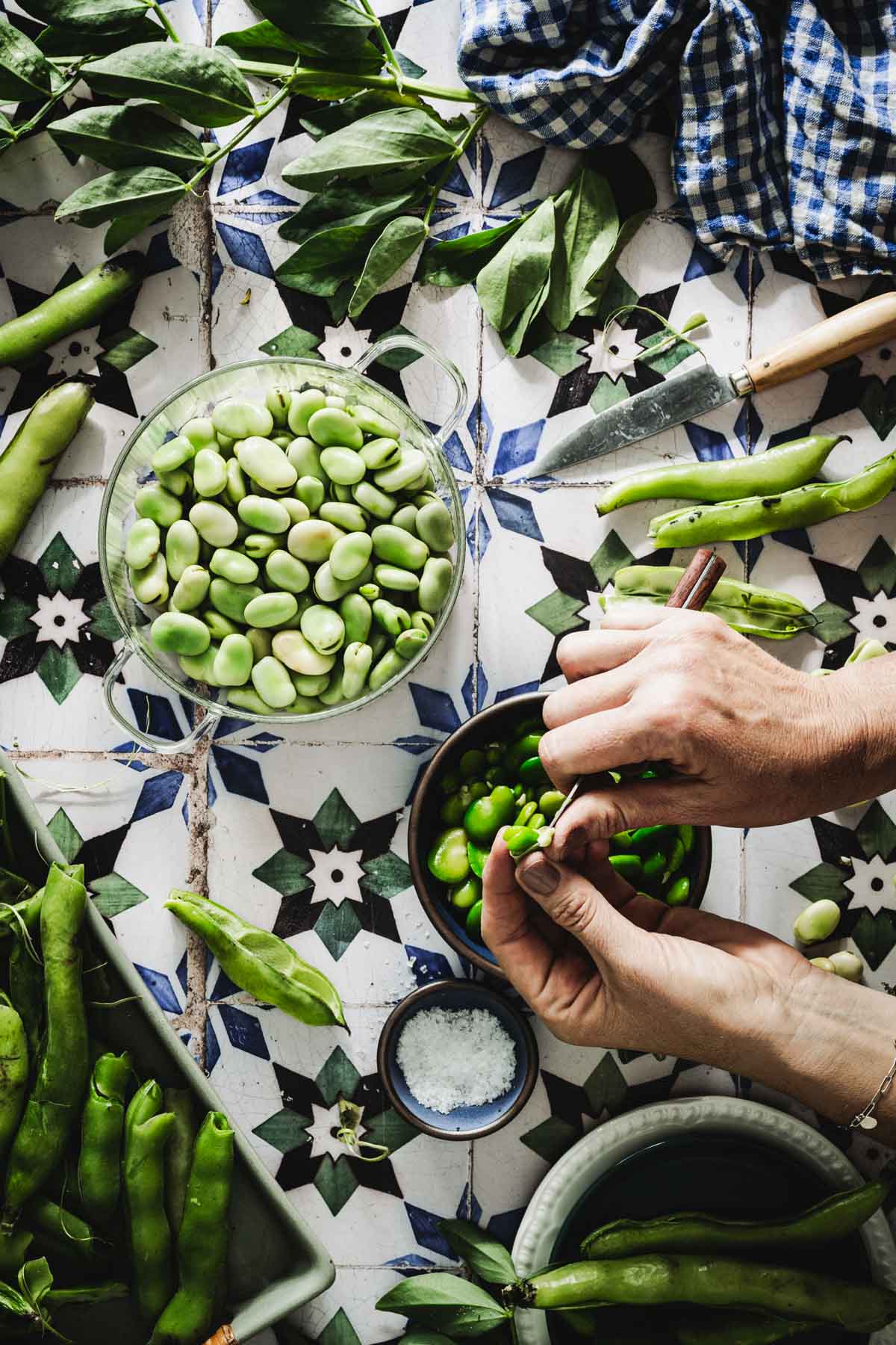 hands in frame holding knife and removing outer shell from the blanched fava beans